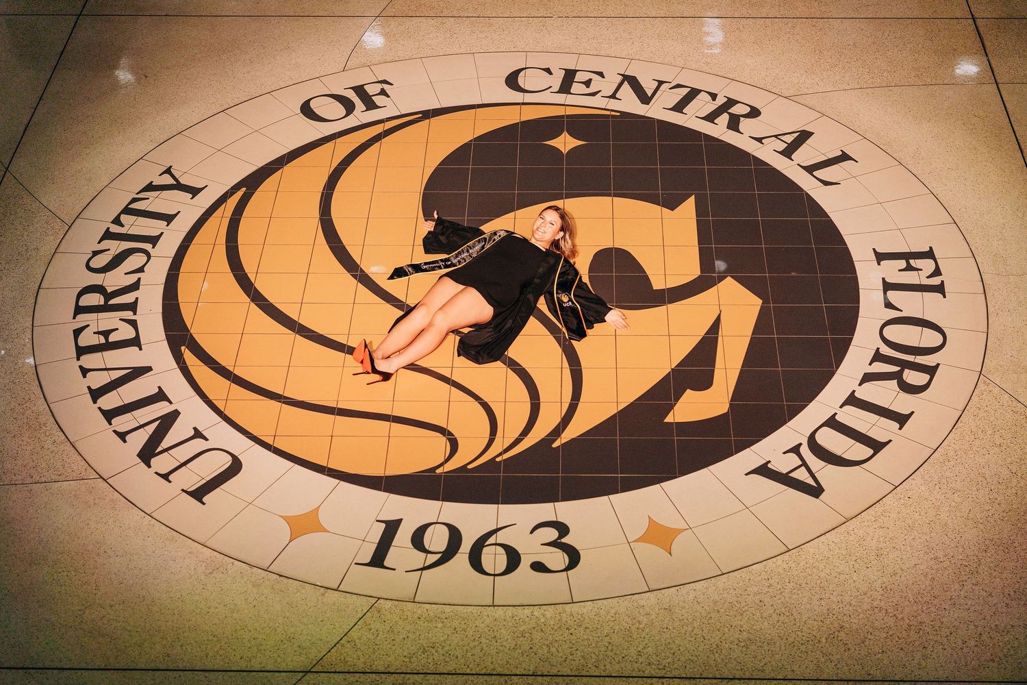Woman posing on the University of Central Florida seal floor mosaic, established 1963, in UCF's main building.
