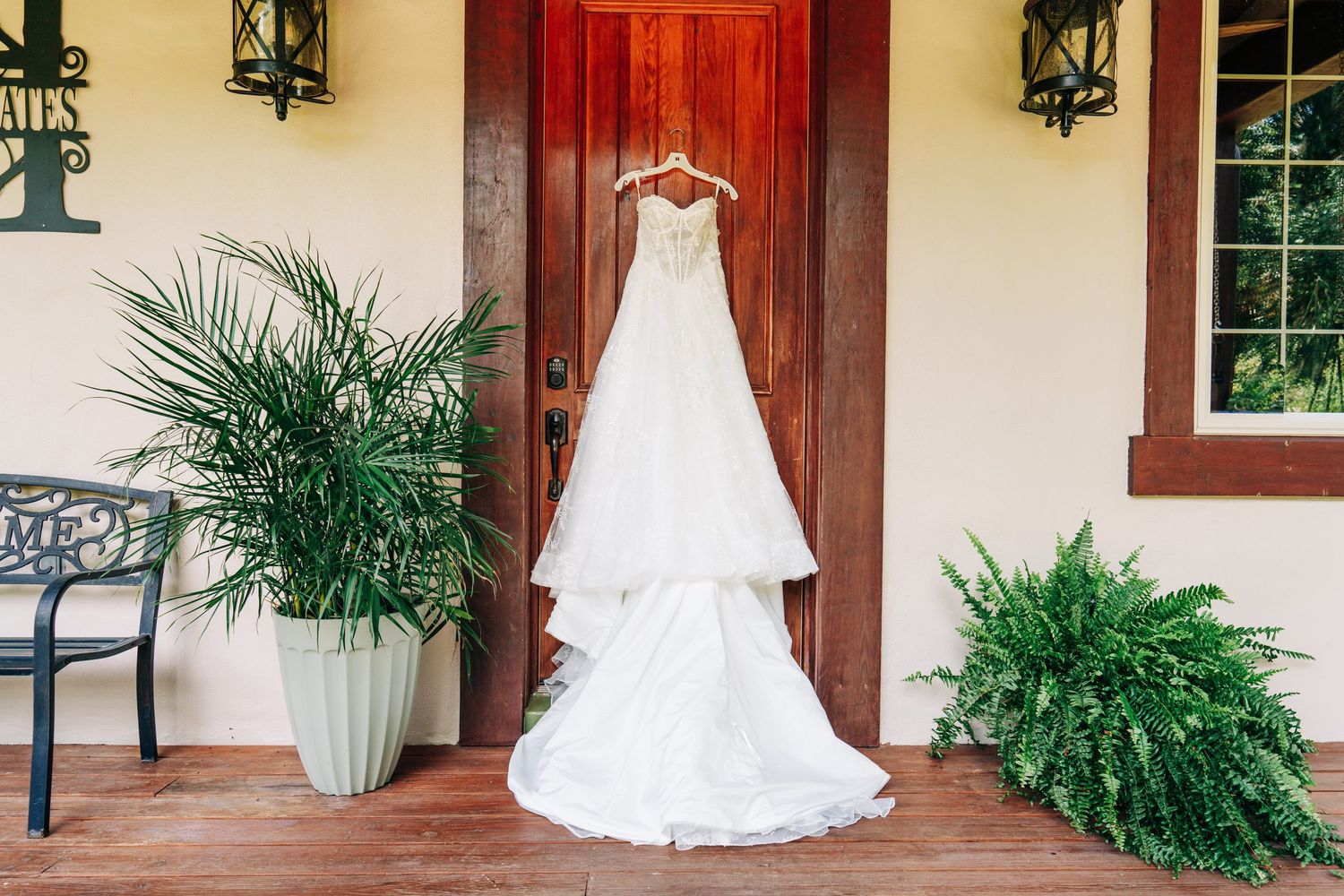 Two wedding dresses hanging on the porch framed by potted palms at Casani Estates, Orlando, Florida wedding venue
