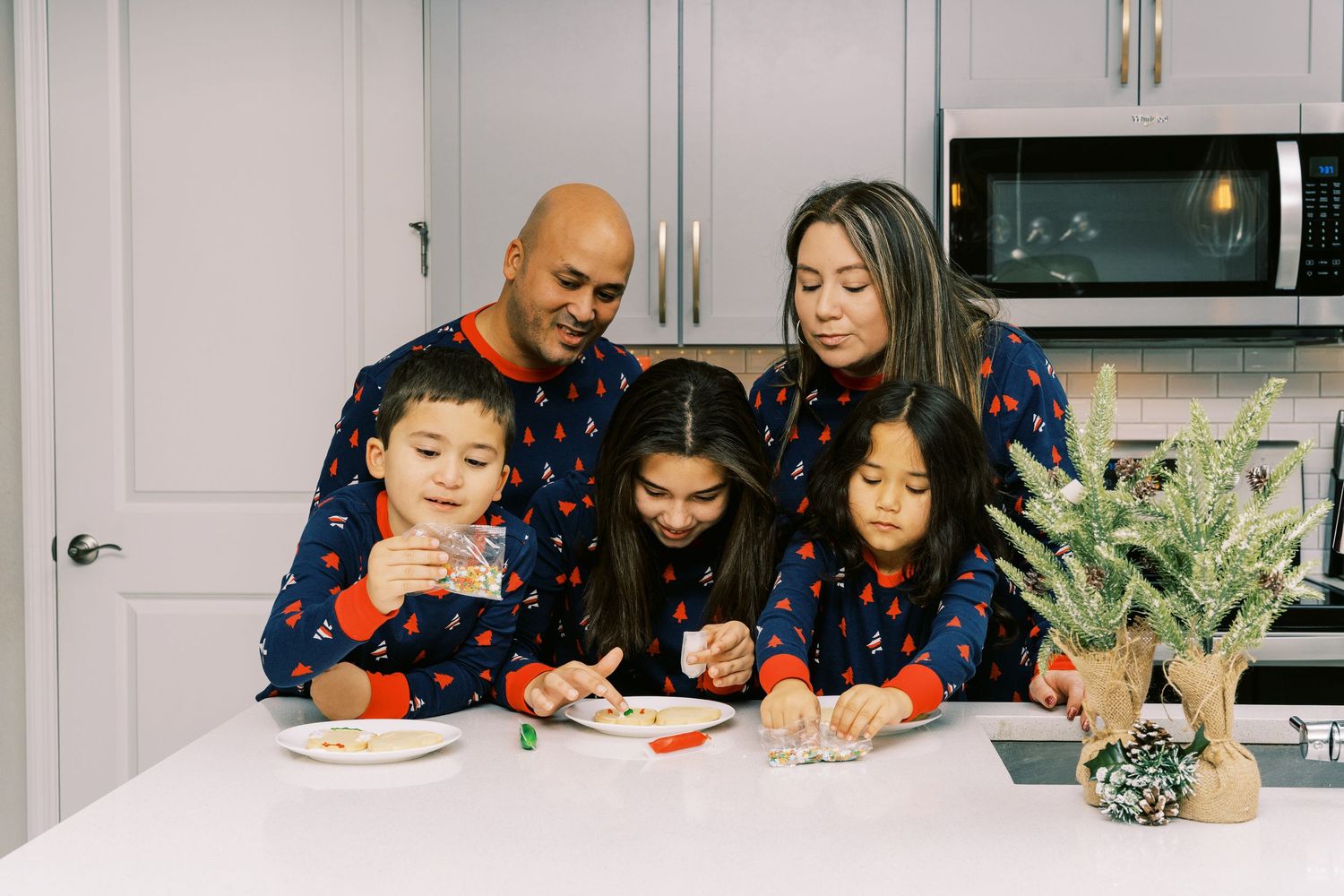 A family gathers around a kitchen counter decorating food items together at home while smiling.