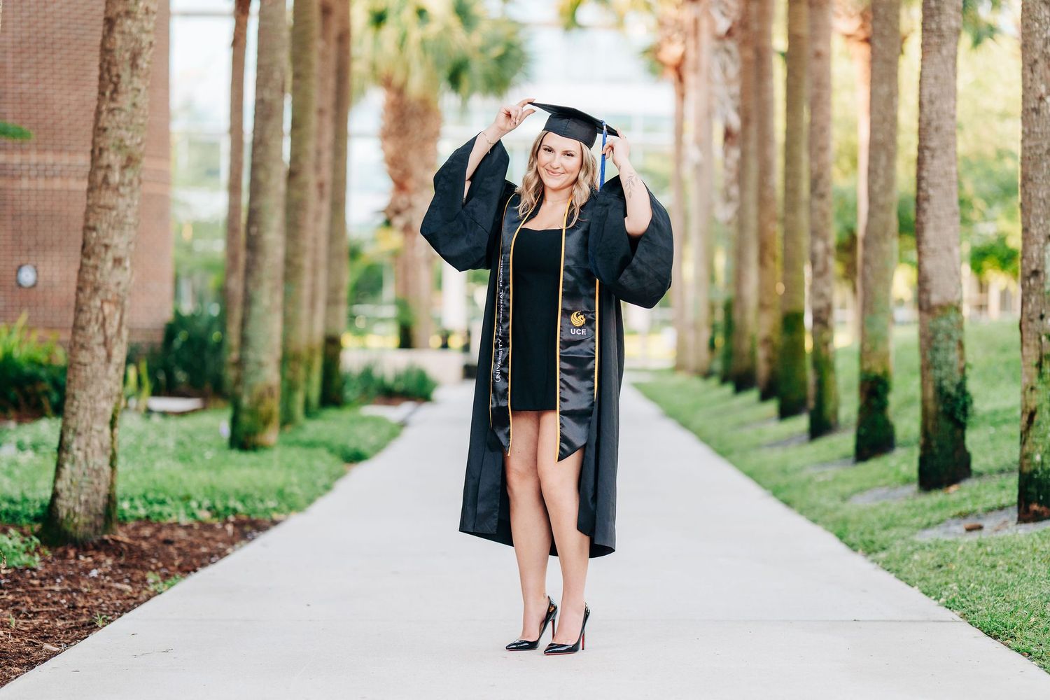 UCF graduate in cap and gown on a palm lined walkway at the University of Central Florida in Orlando