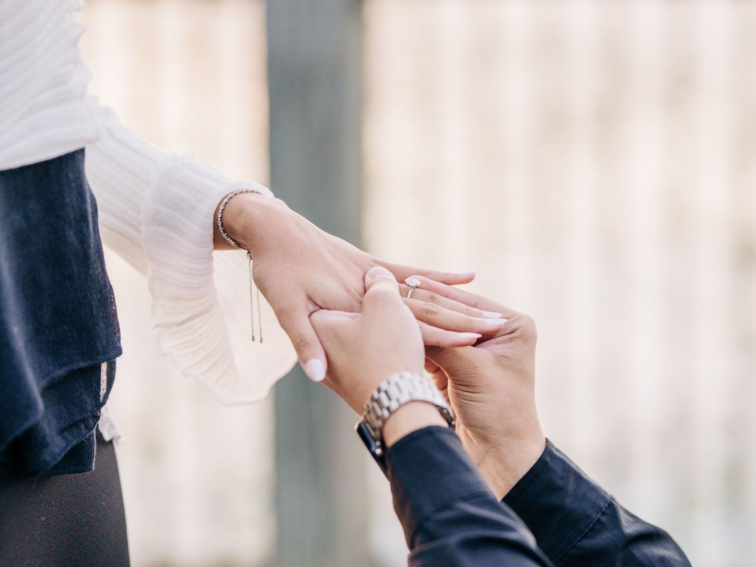 Close up view of two hands coming together in a tender engagement moment with a diamond ring on display.