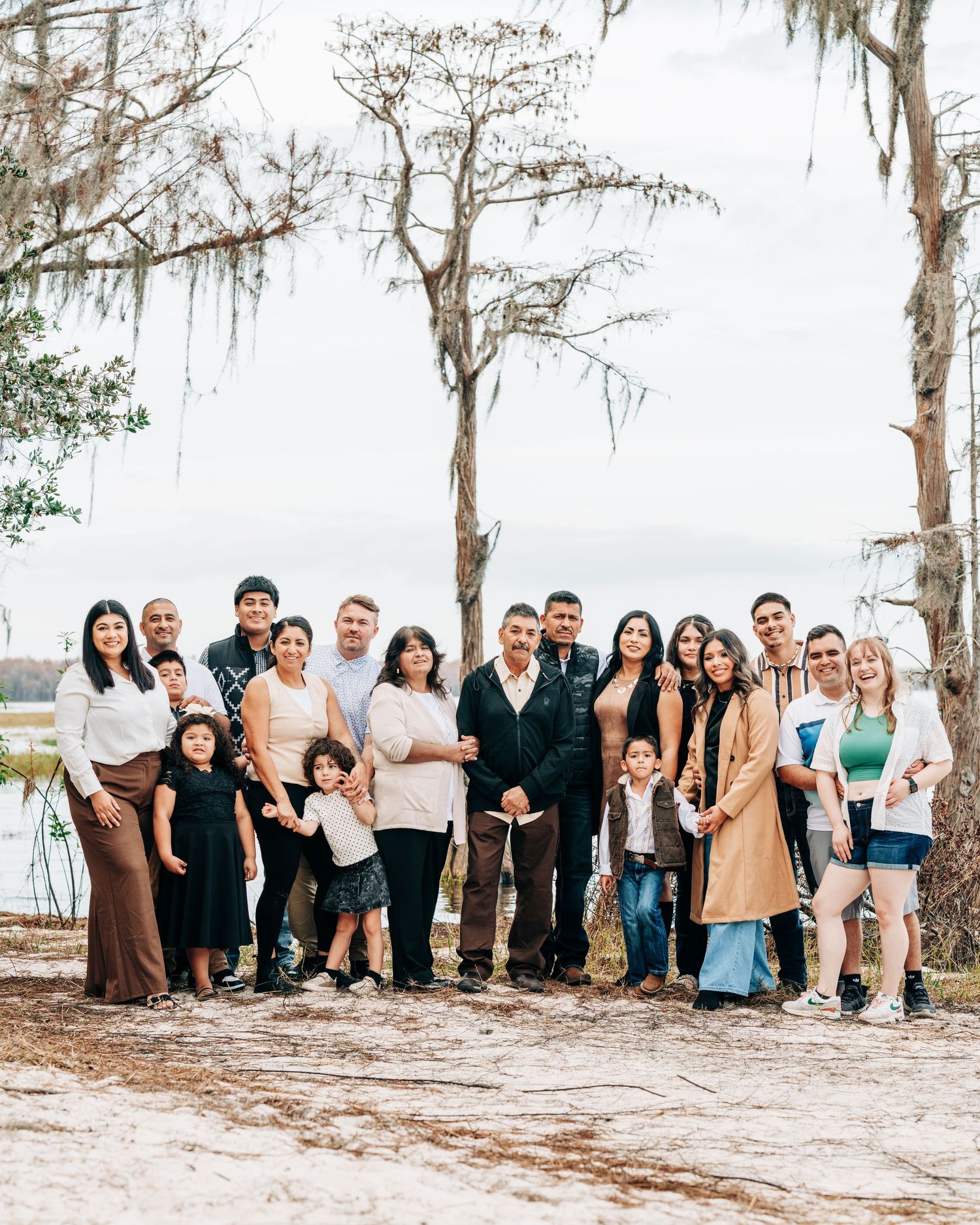 A large group of people gathered outdoors posing together with Spanish moss-covered trees and a lake in the background.