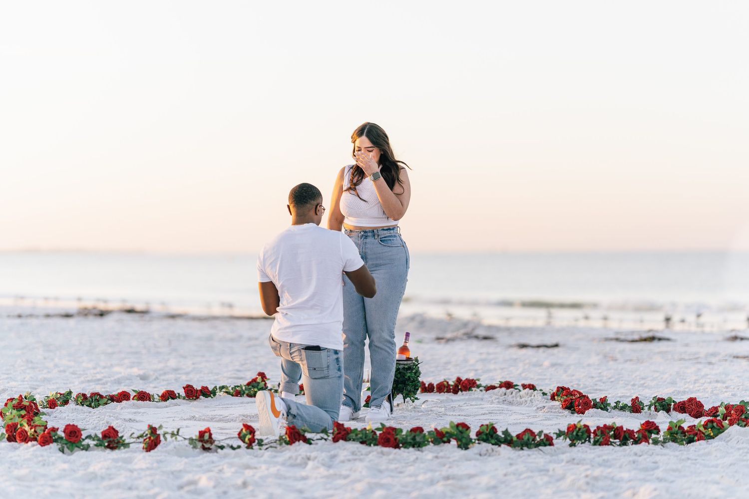 Surprise proposal on one knee inside a heart of red roses at sunset on Siesta Key Beach, Sarasota, Florida