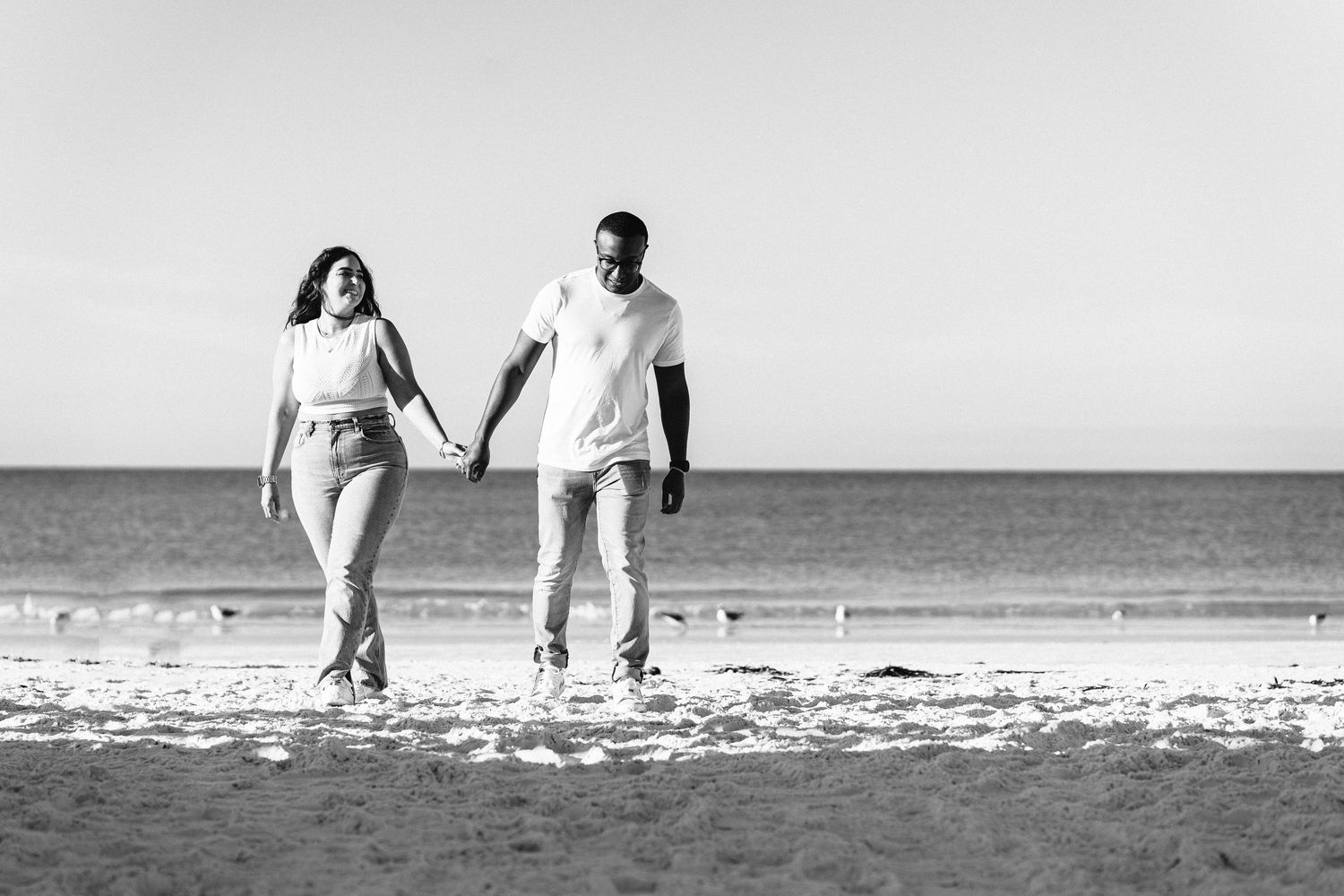 Couple in white walking hand in hand along the shoreline at Siesta Key Beach in Sarasota, Florida engagement photos
