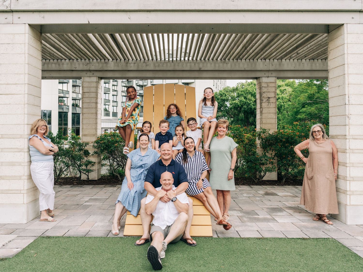 Group photo of people gathered under an outdoor covered porch area with columns and greenery in the background.