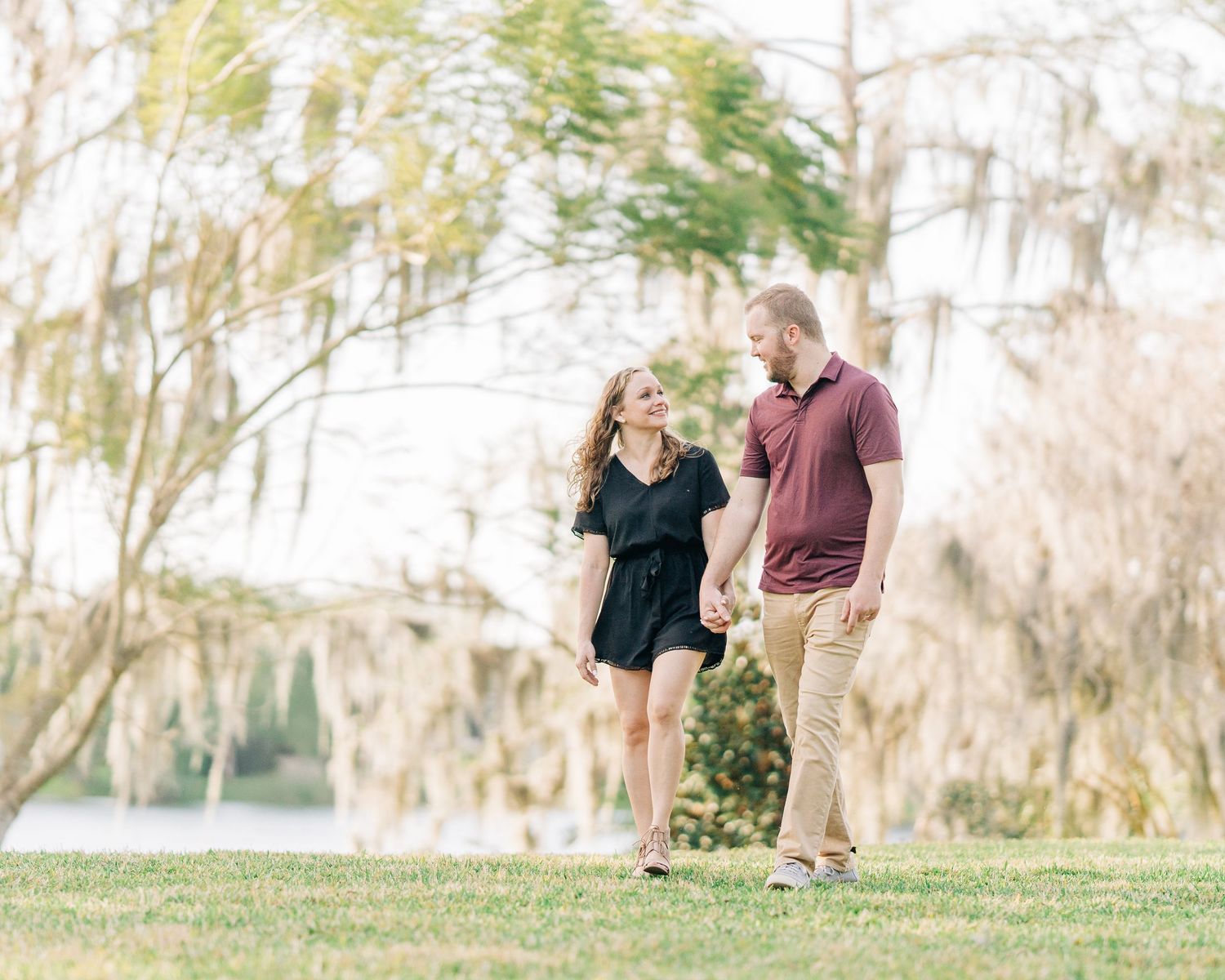 A couple walks together in a romantic outdoor setting with Spanish moss-draped trees in the background.