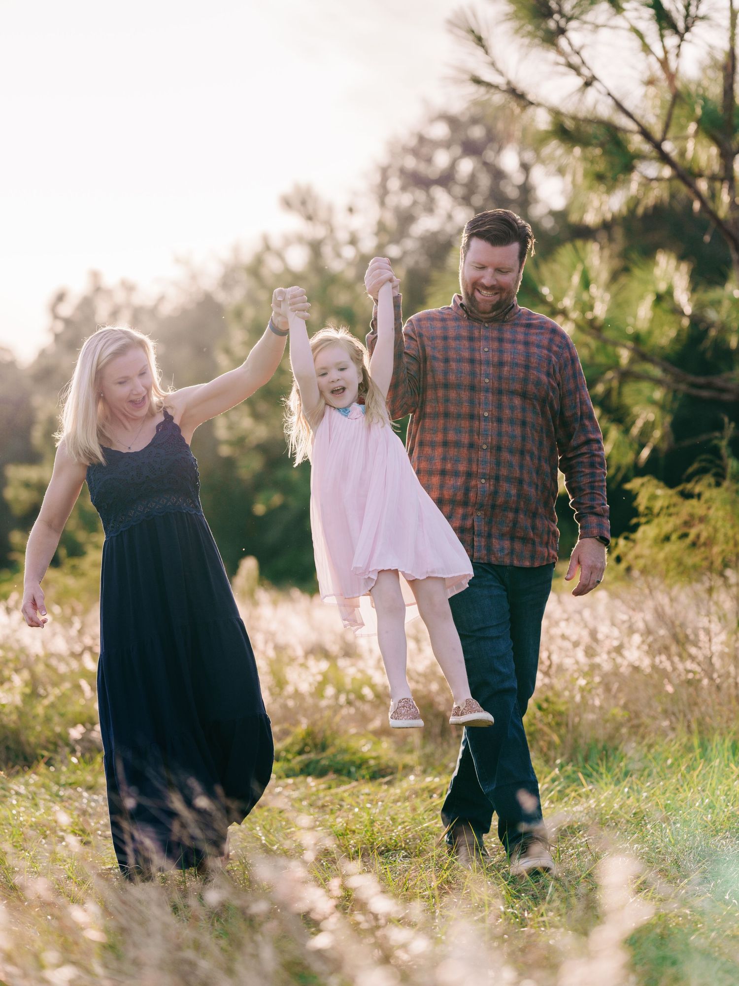 A family joyfully walks through a sunlit meadow of wildflowers during golden hour.