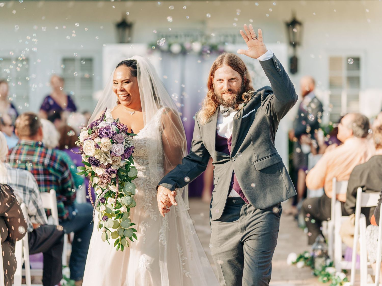 Newlyweds joyfully walk down the aisle together as guests shower them with confetti at an outdoor wedding ceremony.