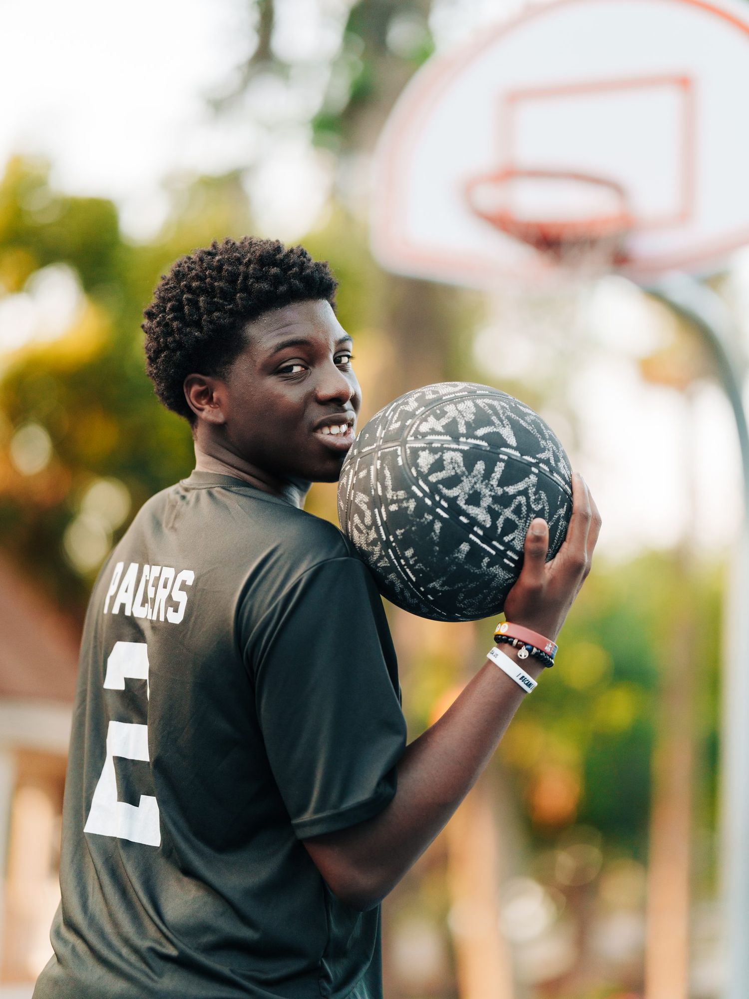 High school senior in a black basketball jersey holding a decorated ball on the court at Speer Park in Oakland, Florida