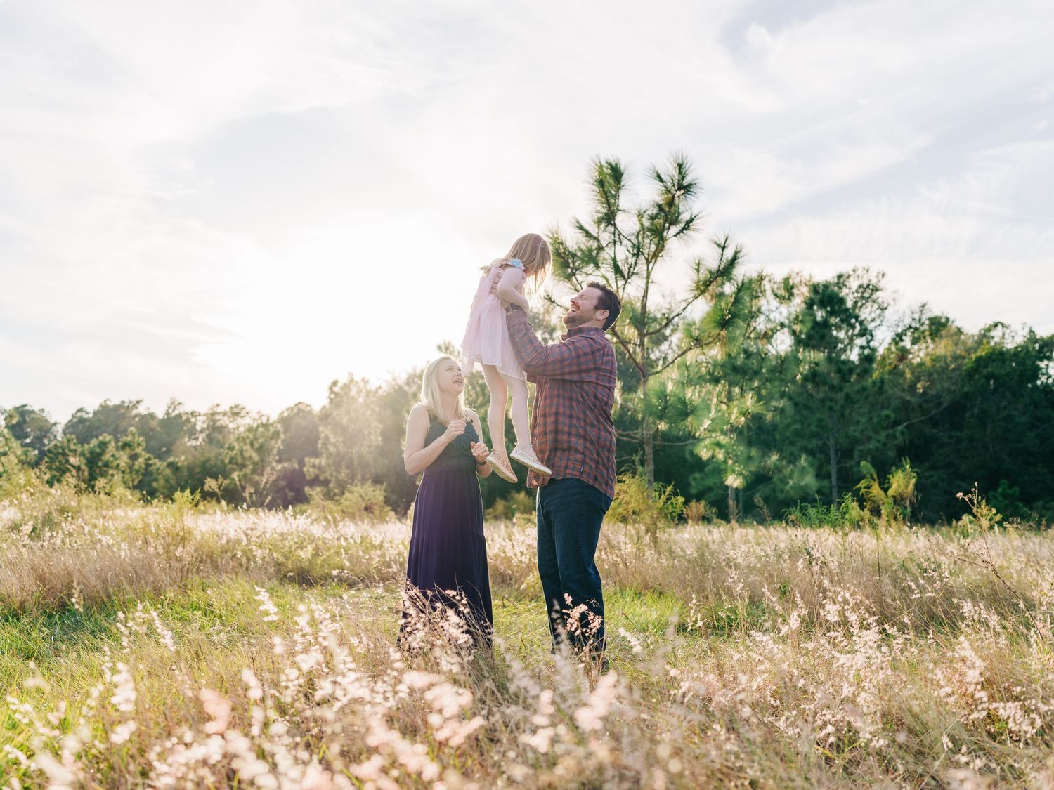 Dreamy sunlit meadow scene with figures embracing among wildflowers and trees during golden hour.