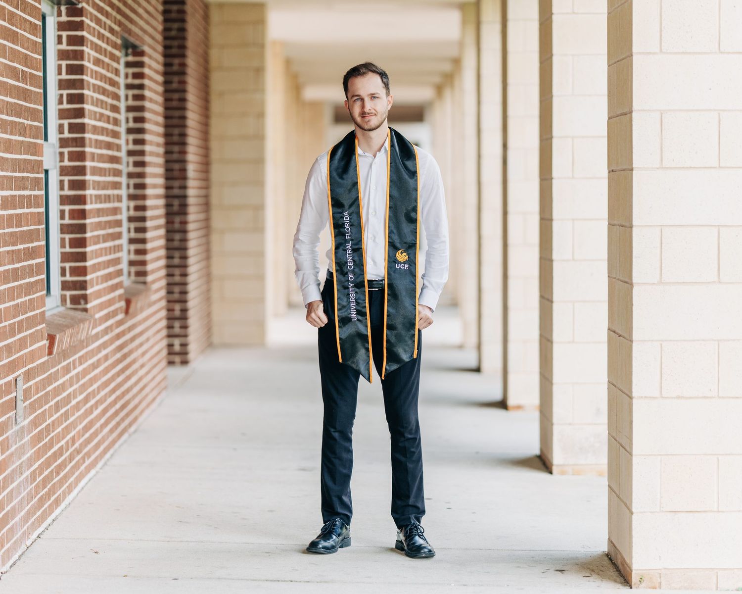 UCF graduate in a gray blazer and navy stole in a brick colonnade, University of Central Florida graduation photos