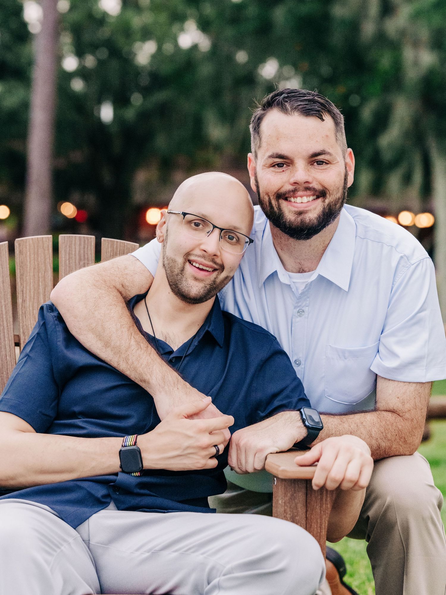 Two people smiling while sitting together on outdoor patio furniture at dusk with bokeh lights in background.