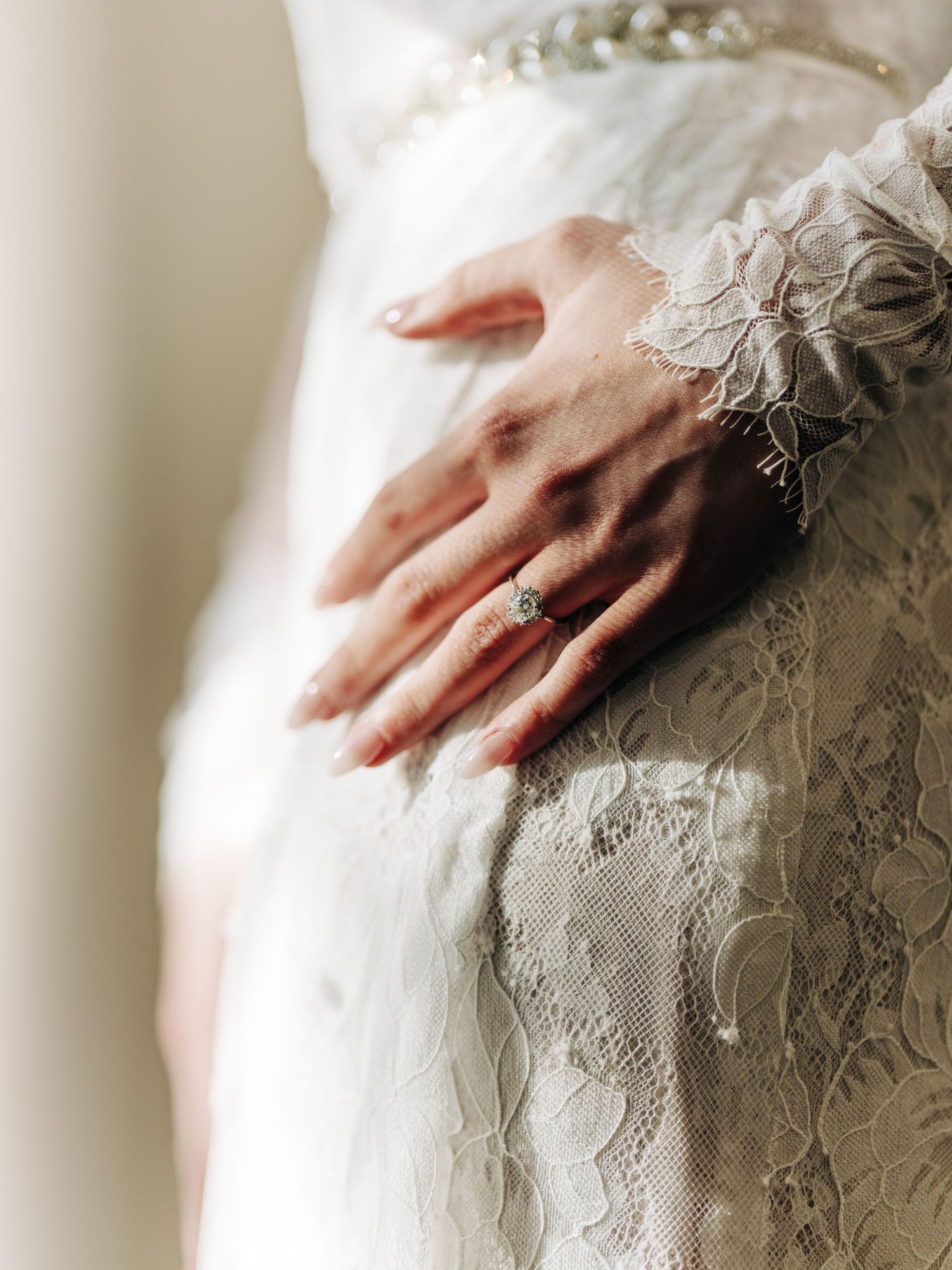 Close-up of an elegant hand wearing a wedding ring against delicate lace and white fabric.