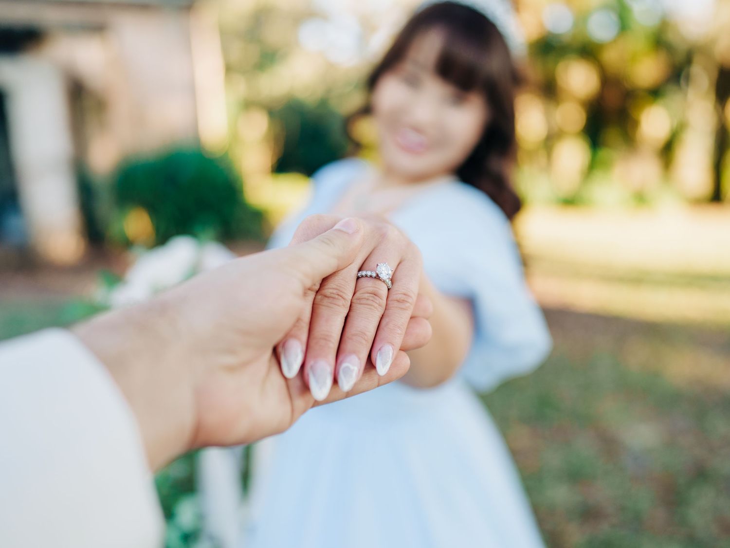 Close up of hands holding and showing off engagement ring in sunlit outdoor garden setting.