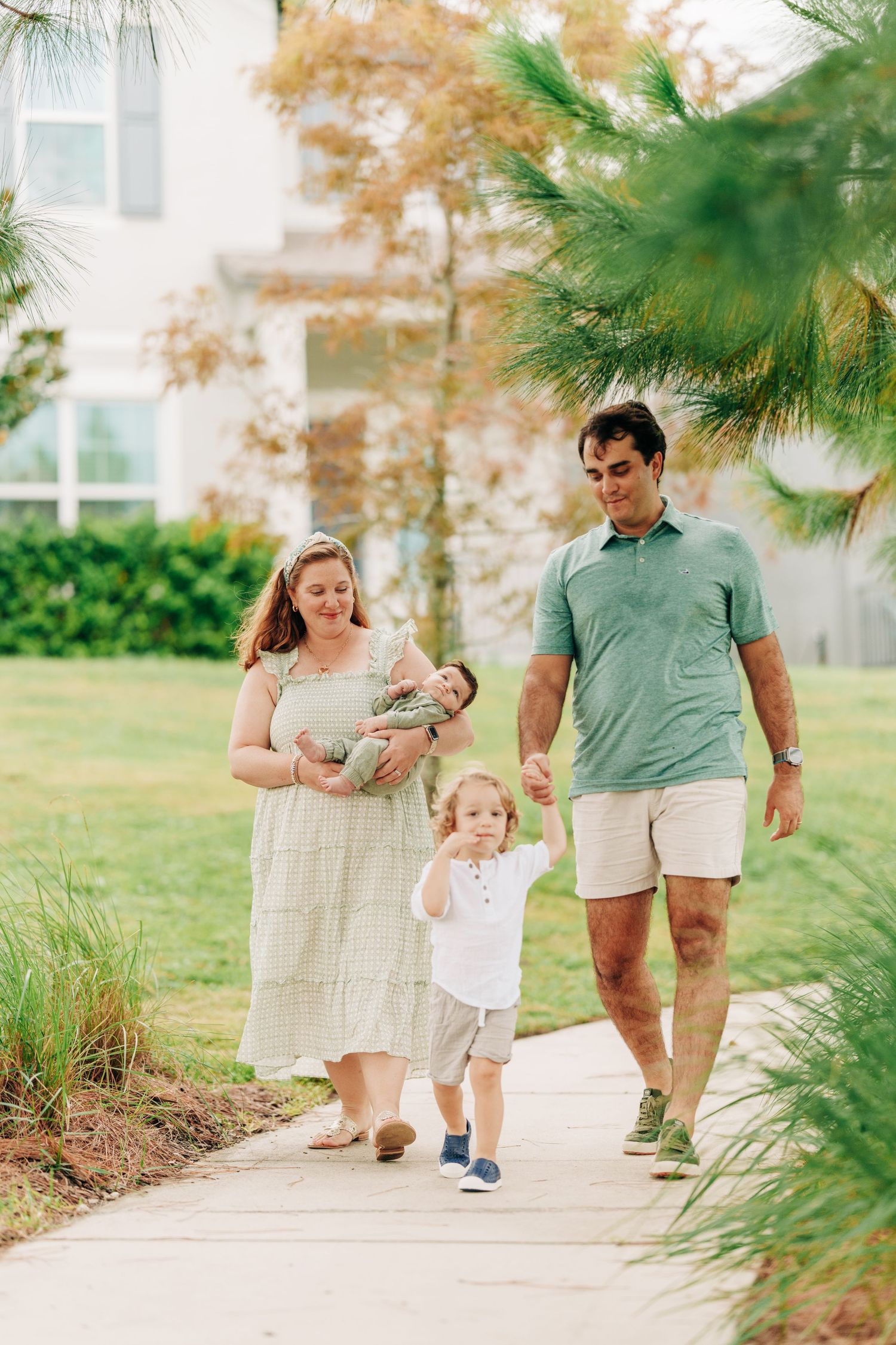 A family walks together on a palm-lined path on a sunny day, with trees and greenery in the background.