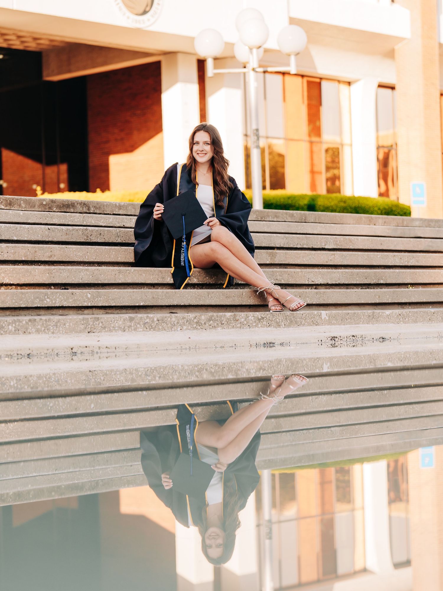 Creative outdoor portrait with reflection in puddle of woman sitting on concrete steps at sunset.