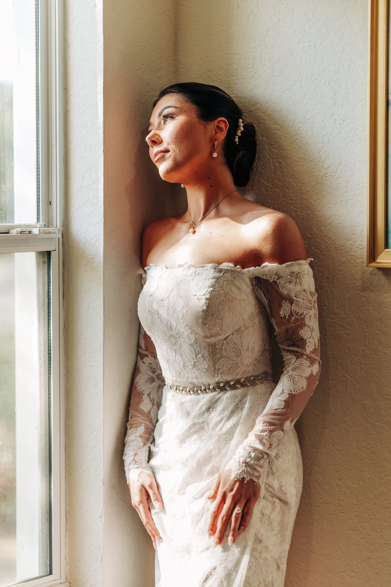 Bride in an off-shoulder lace gown by the window at Sterling Event Venue in Minneola, Florida wedding photography