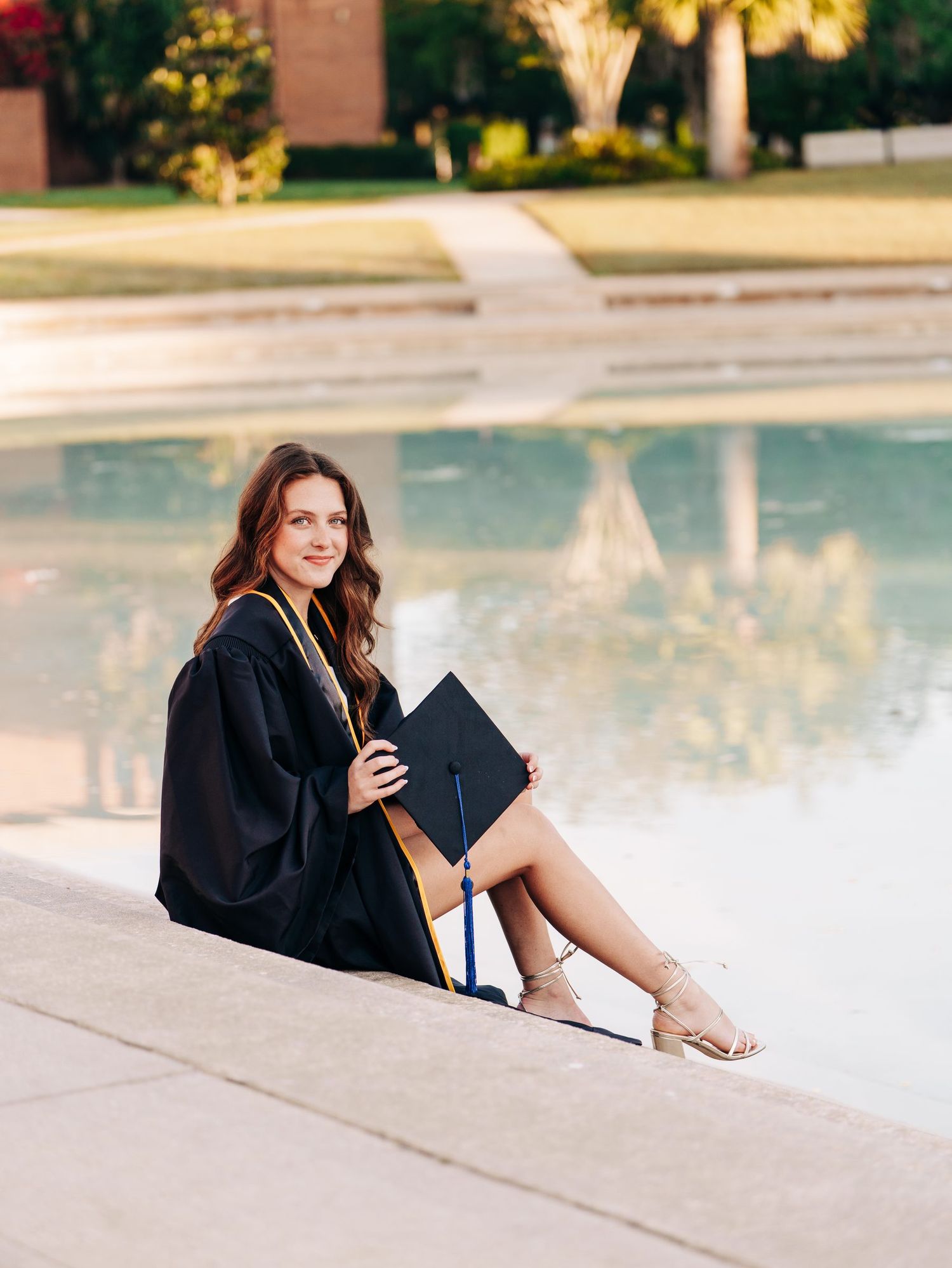 UCF graduate in cap and gown seated by the Reflecting Pond at sunset, University of Central Florida graduation photos