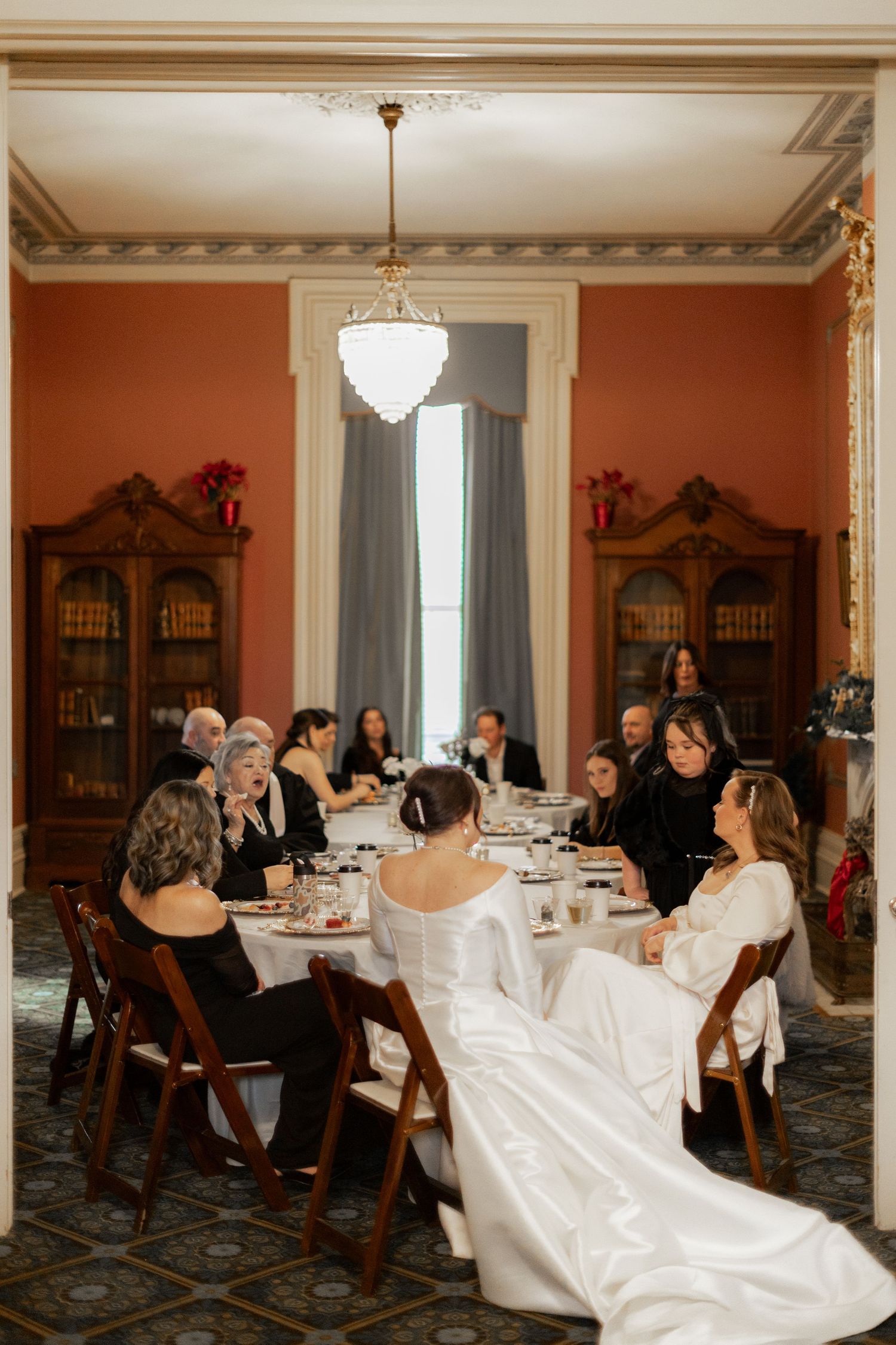 Formal dining room with crystal chandelier and guests seated at tables covered in white linens.