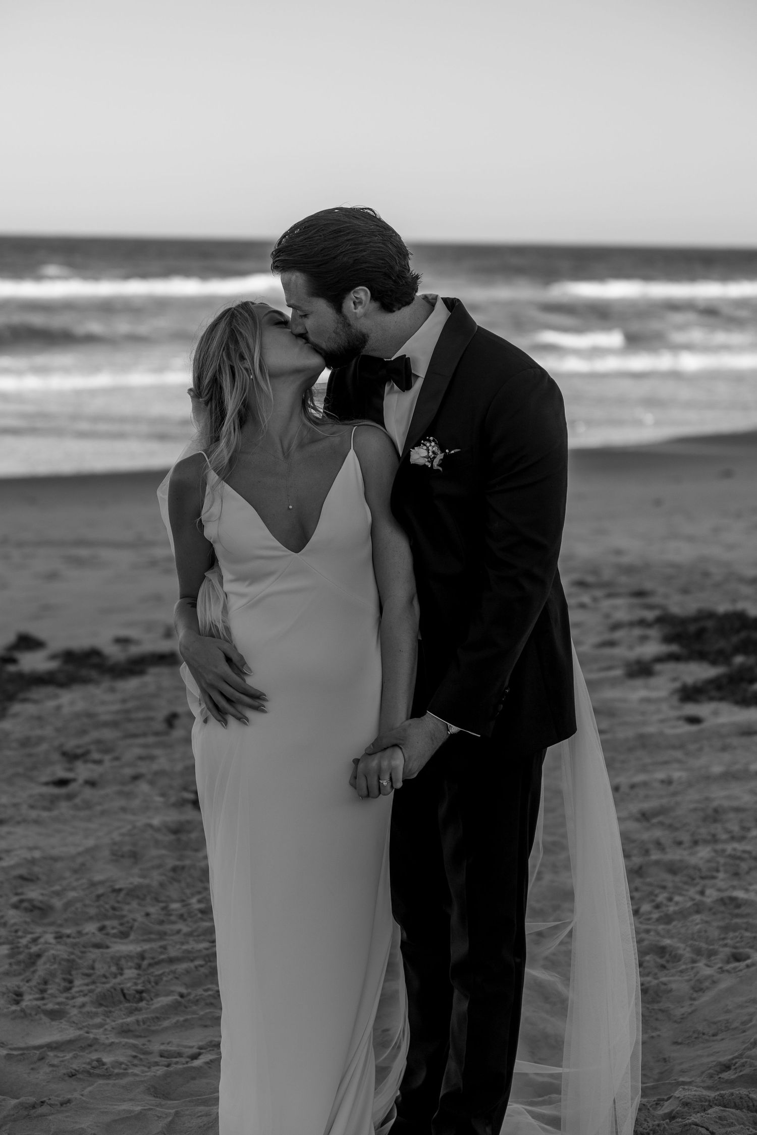 A romantic black and white portrait of newlyweds sharing an intimate moment on the beach.