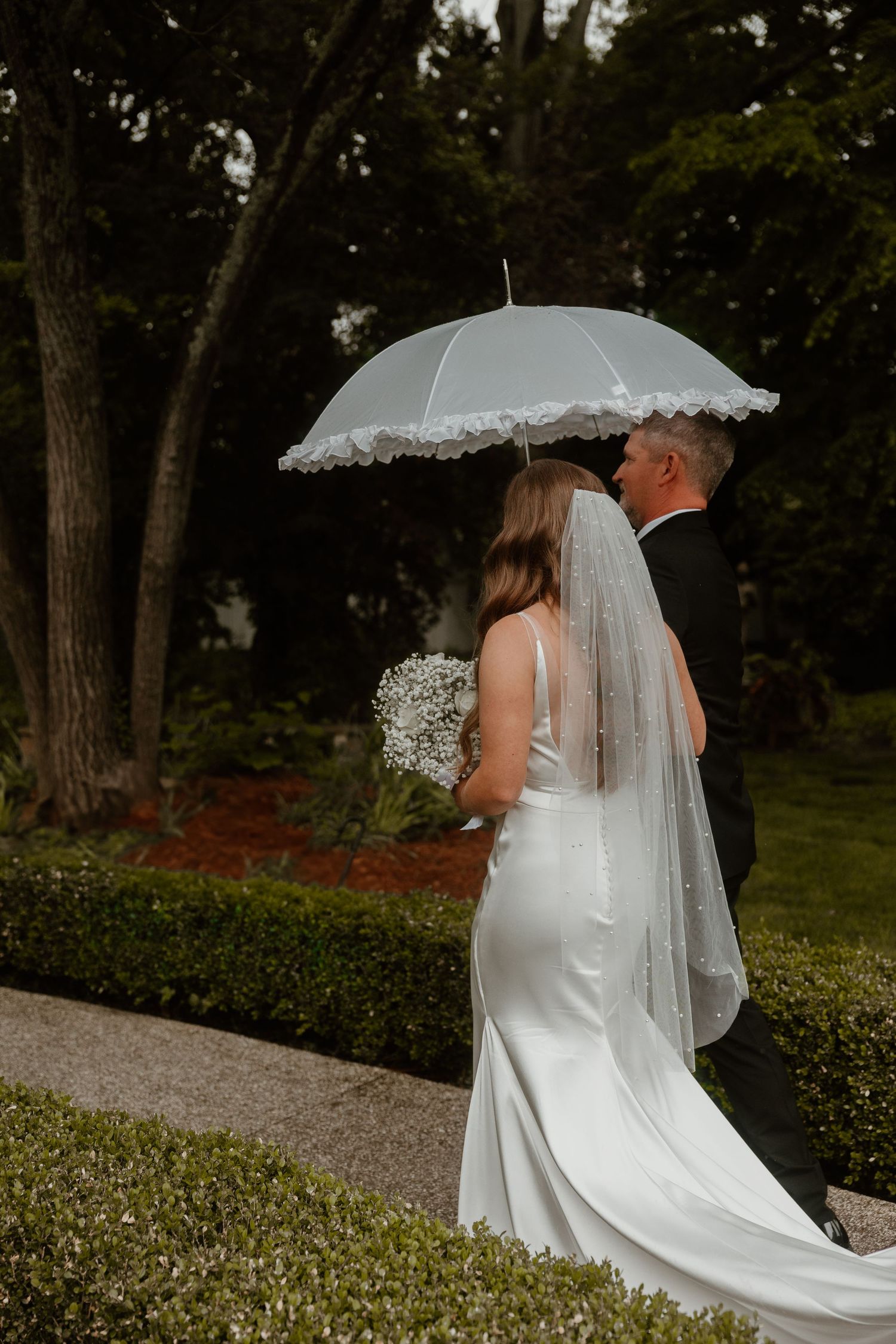 A couple stands under a white lace umbrella during their outdoor wedding ceremony.