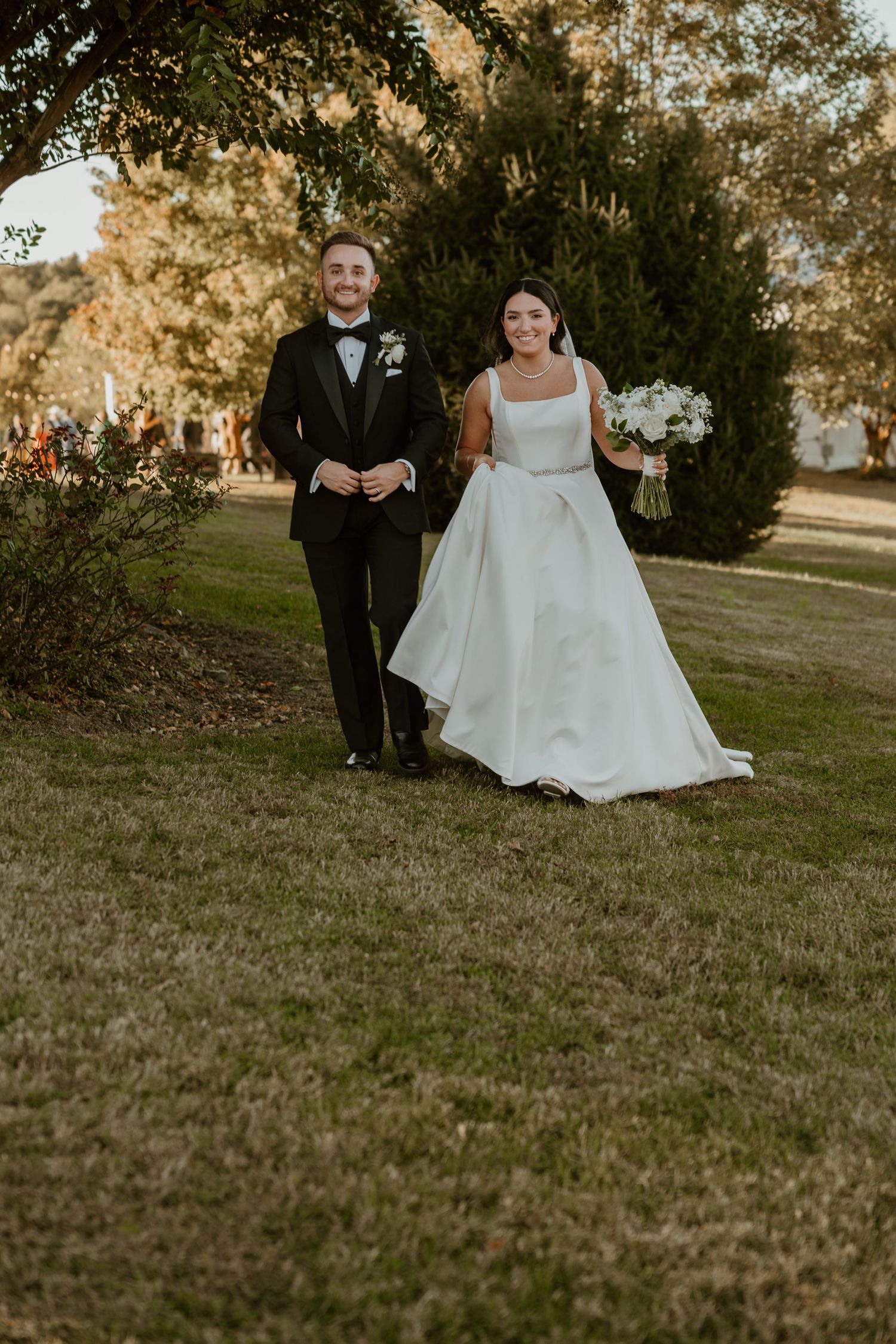 A couple walking on grass during their wedding, the bride in a white ballgown and groom in a black tuxedo.