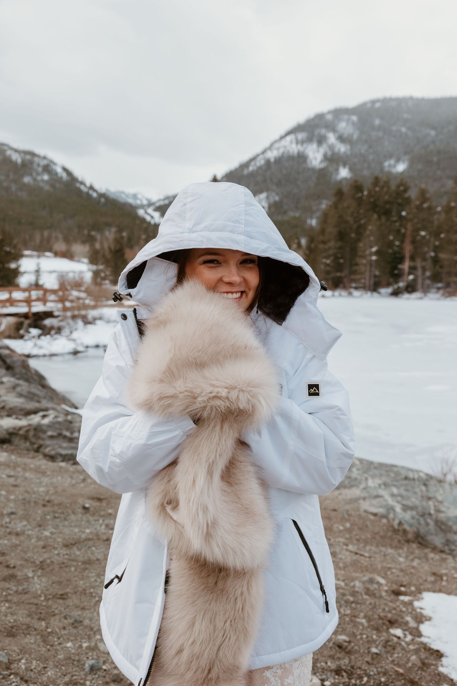 A winter bride in a white puffer jacket and fur scarf poses in the snow.