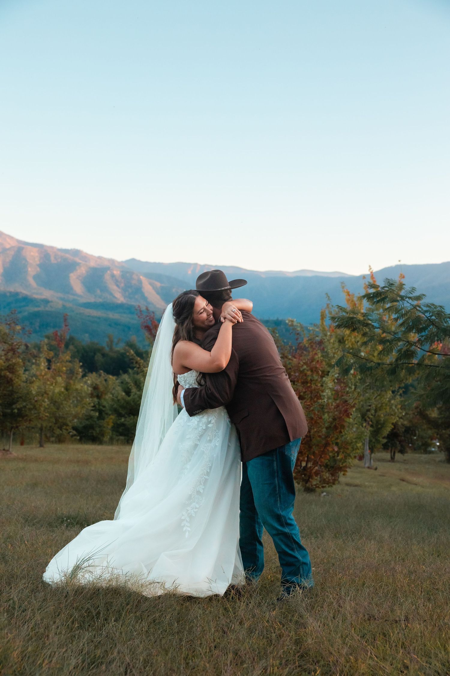 A couple shares a playful moment in a mountain meadow during their wedding photoshoot.