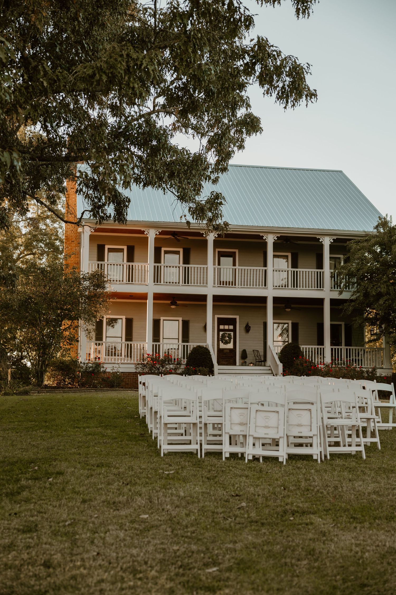 Southern plantation style house with white chairs set up for outdoor wedding ceremony.
