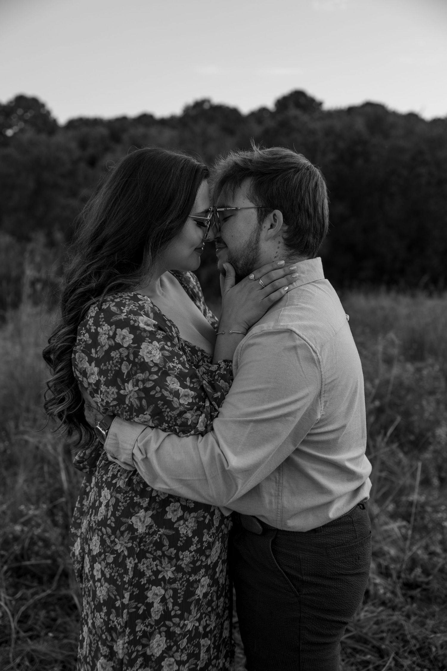 Black and white portrait of couple sharing romantic moment in wild meadow at sunset.