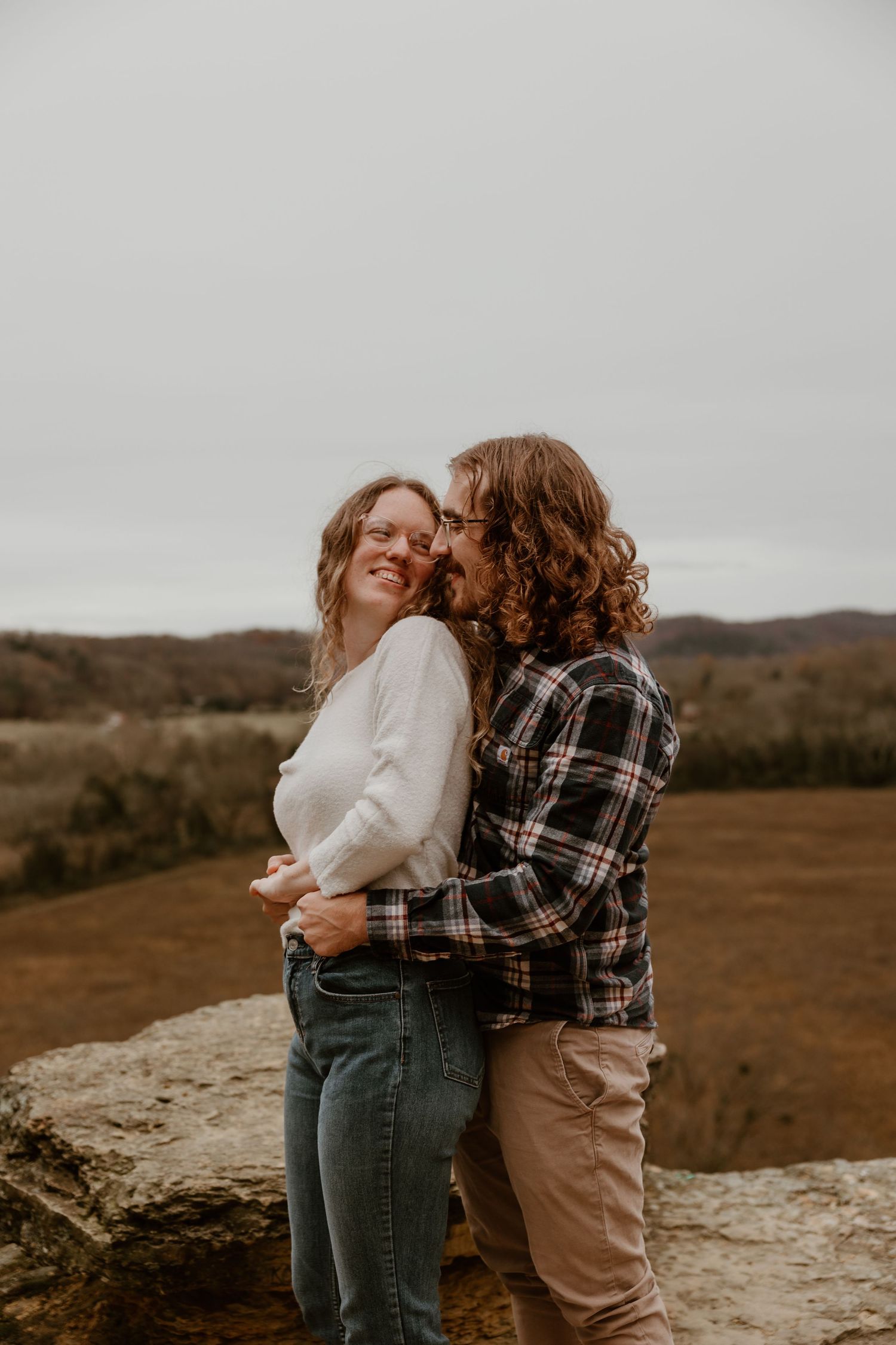 Two people sharing an intimate moment on a rocky outcrop overlooking a natural landscape.