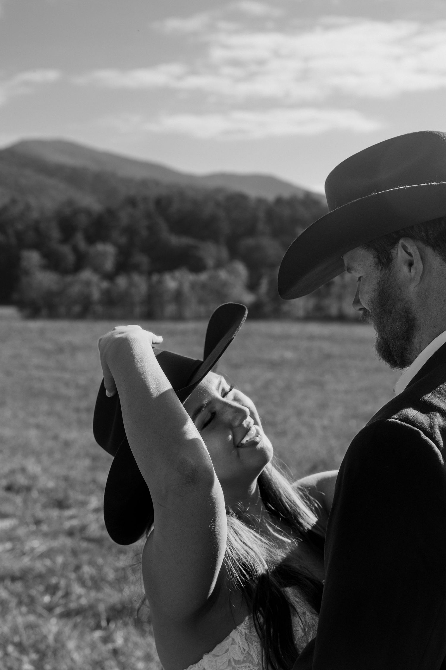 A romantic black and white photo of a couple in a field with mountains in the background.