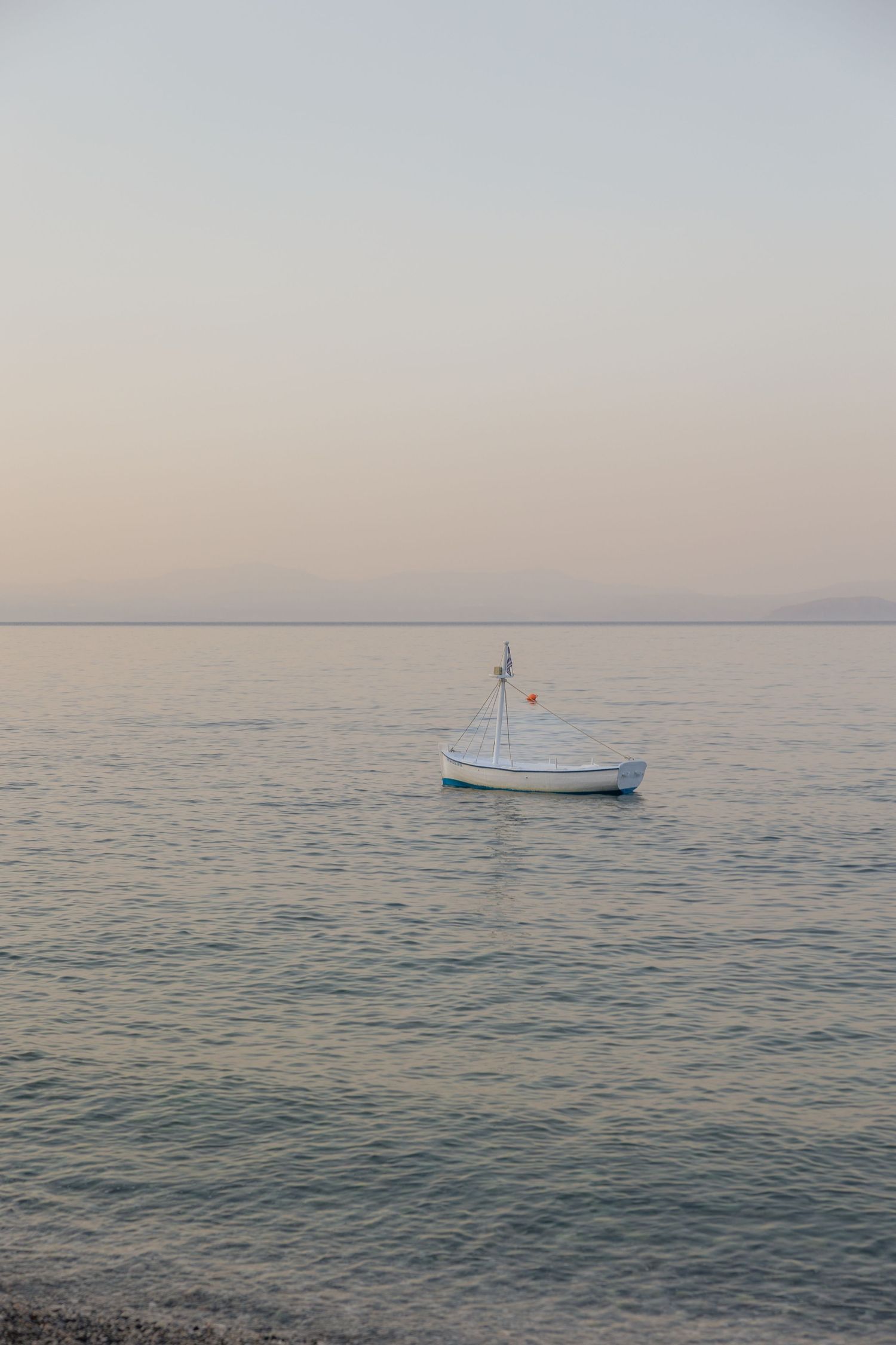 A small white boat floats peacefully on calm blue waters during a misty sunset.