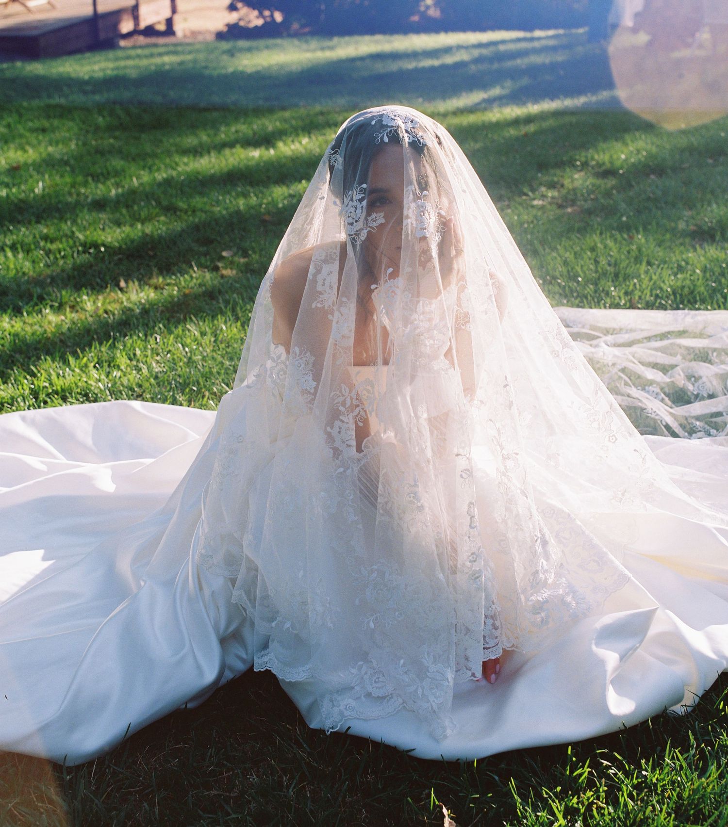 A flowing white wedding dress train spreads across green grass in natural outdoor lighting.