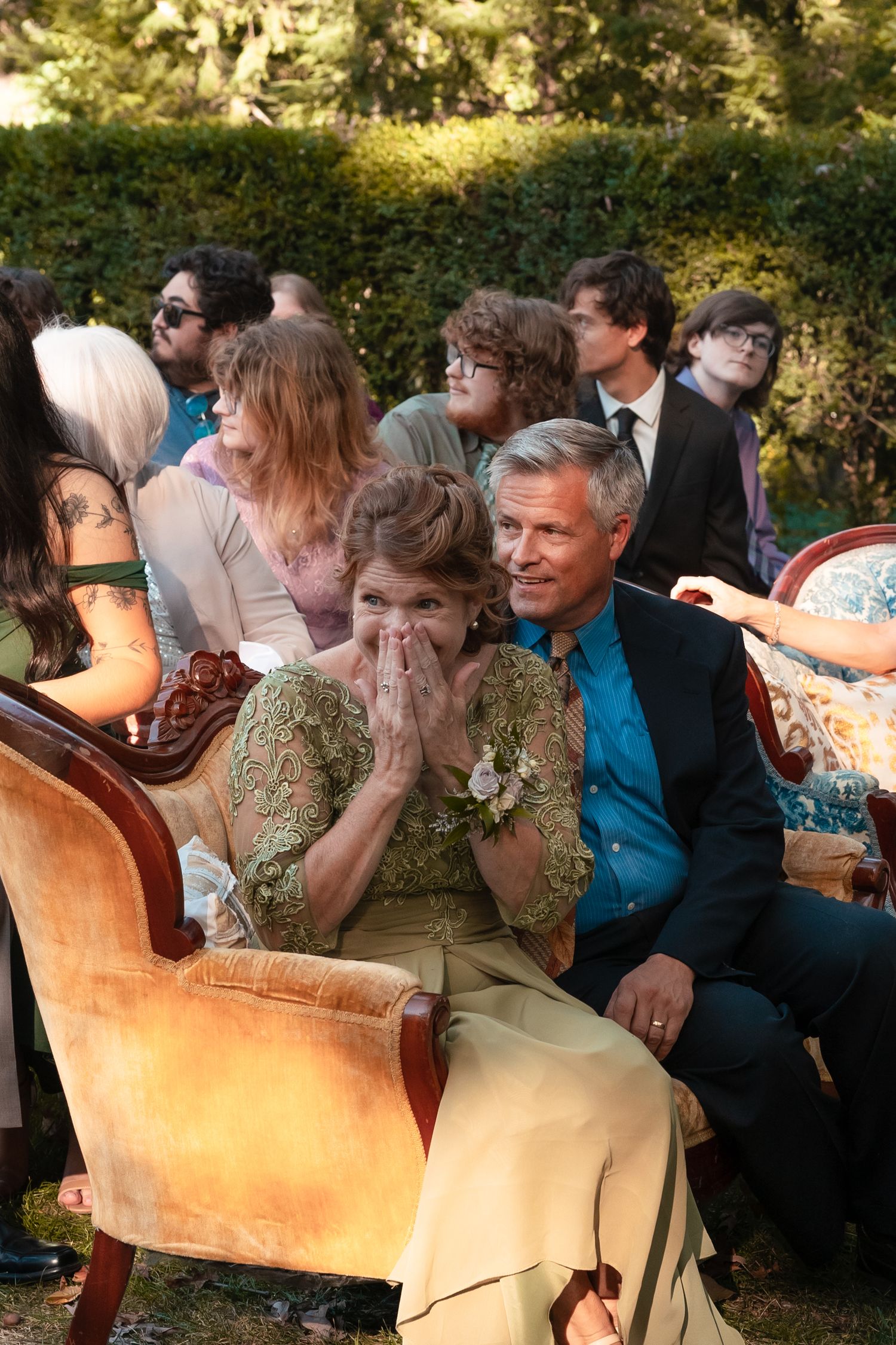 A group of people sitting on a vintage couch outdoors share a joyful moment during a social gathering.