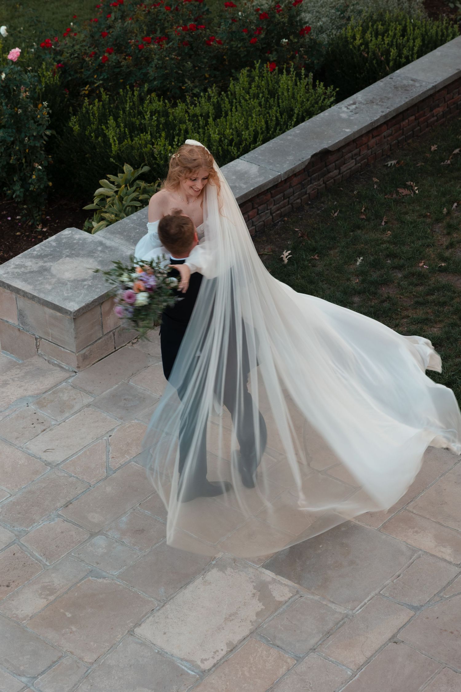 Couple in wedding attire sharing an intimate moment on stone patio steps.