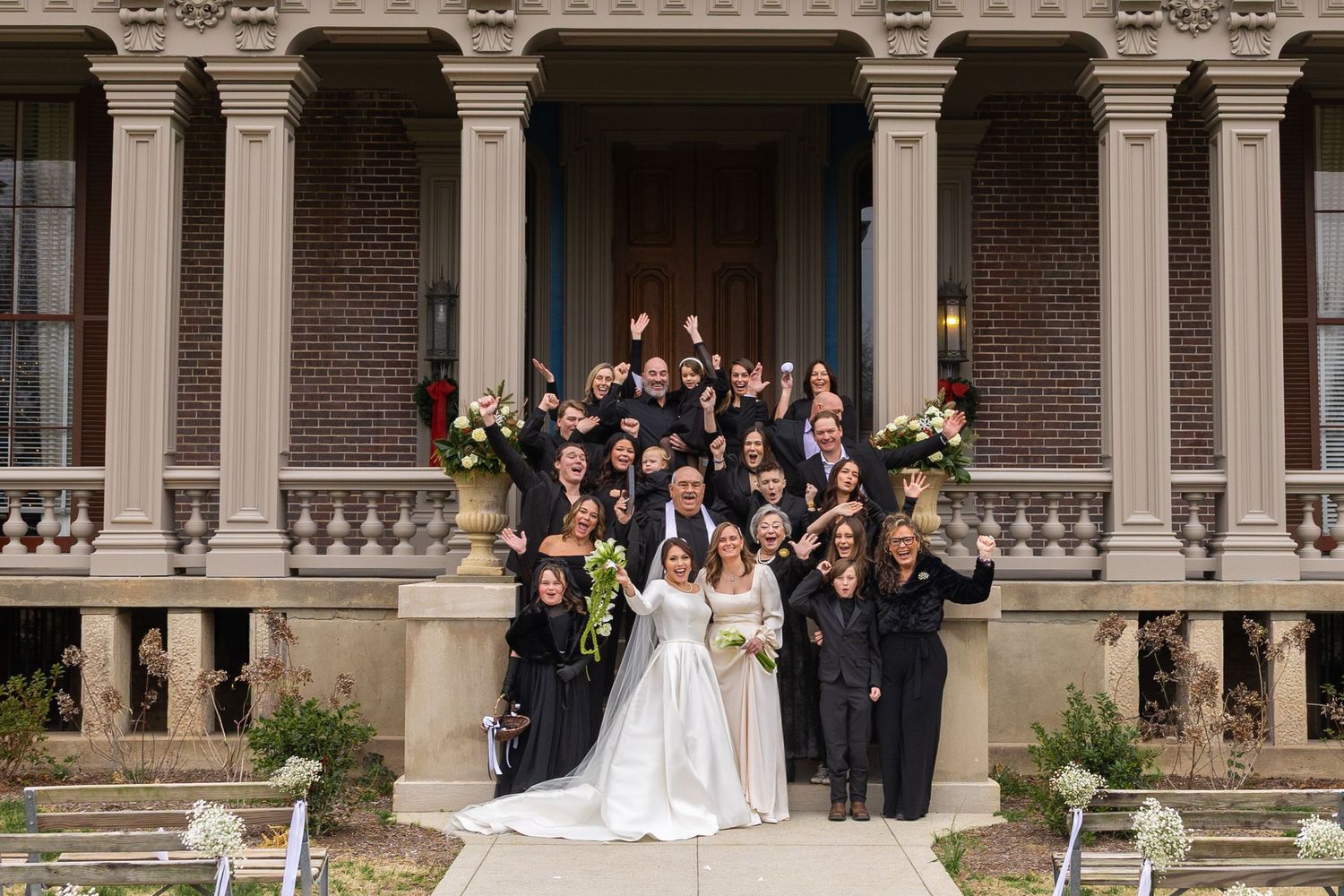 Wedding party poses on grand steps of historic mansion with ornate columns and architecture.