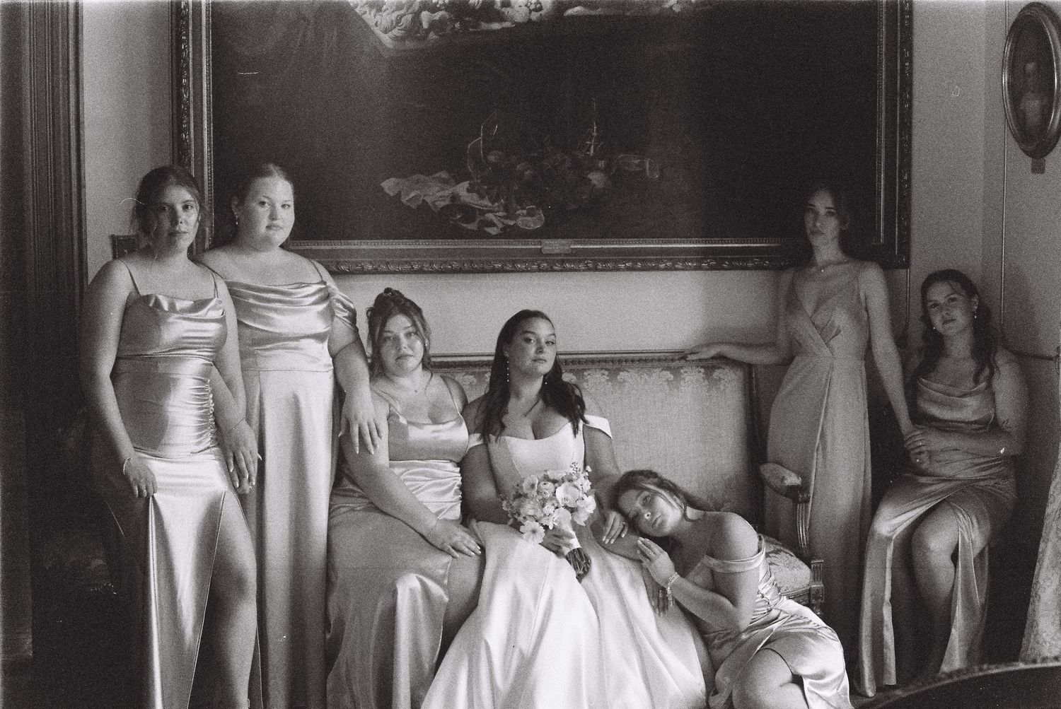 A wedding party of bridesmaids in matching dresses gather indoors for a formal photo.