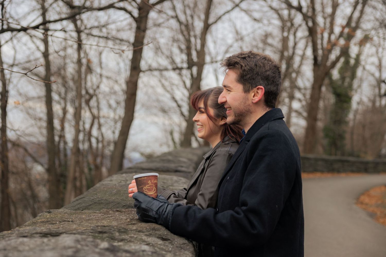 A couple walks together on a tree-lined path during autumn with bare branches overhead.
