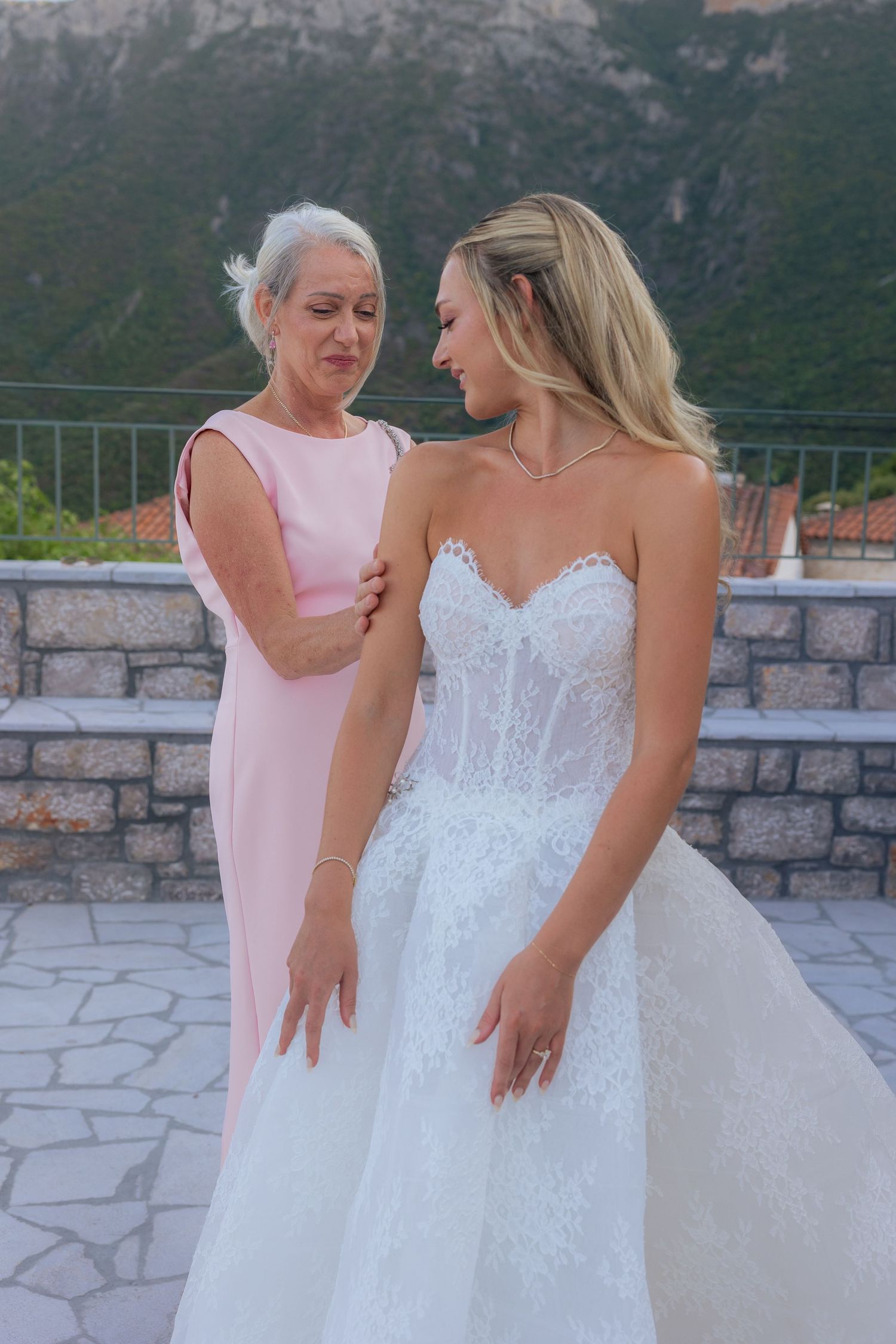 Two people share a joyful moment on a stone terrace with mountains in the background.