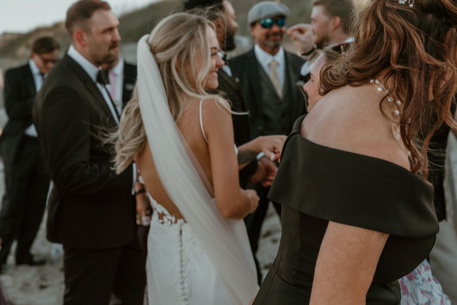 Wedding guests gather around on a beach during an intimate celebration.