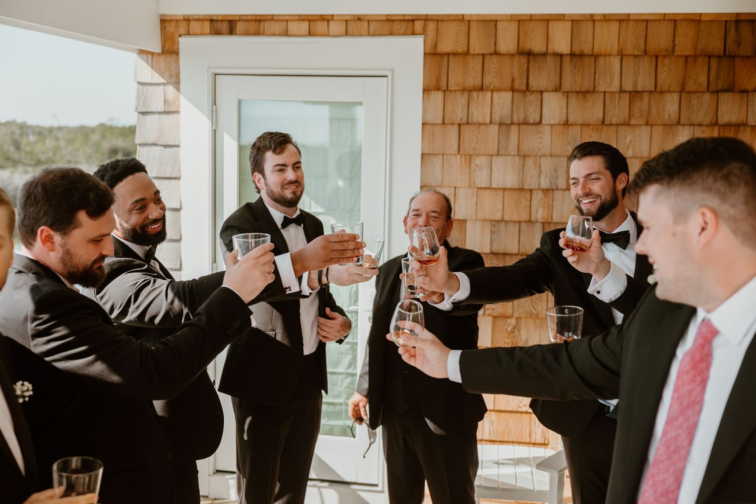 Wedding party in formal attire raising glasses for a celebratory toast.