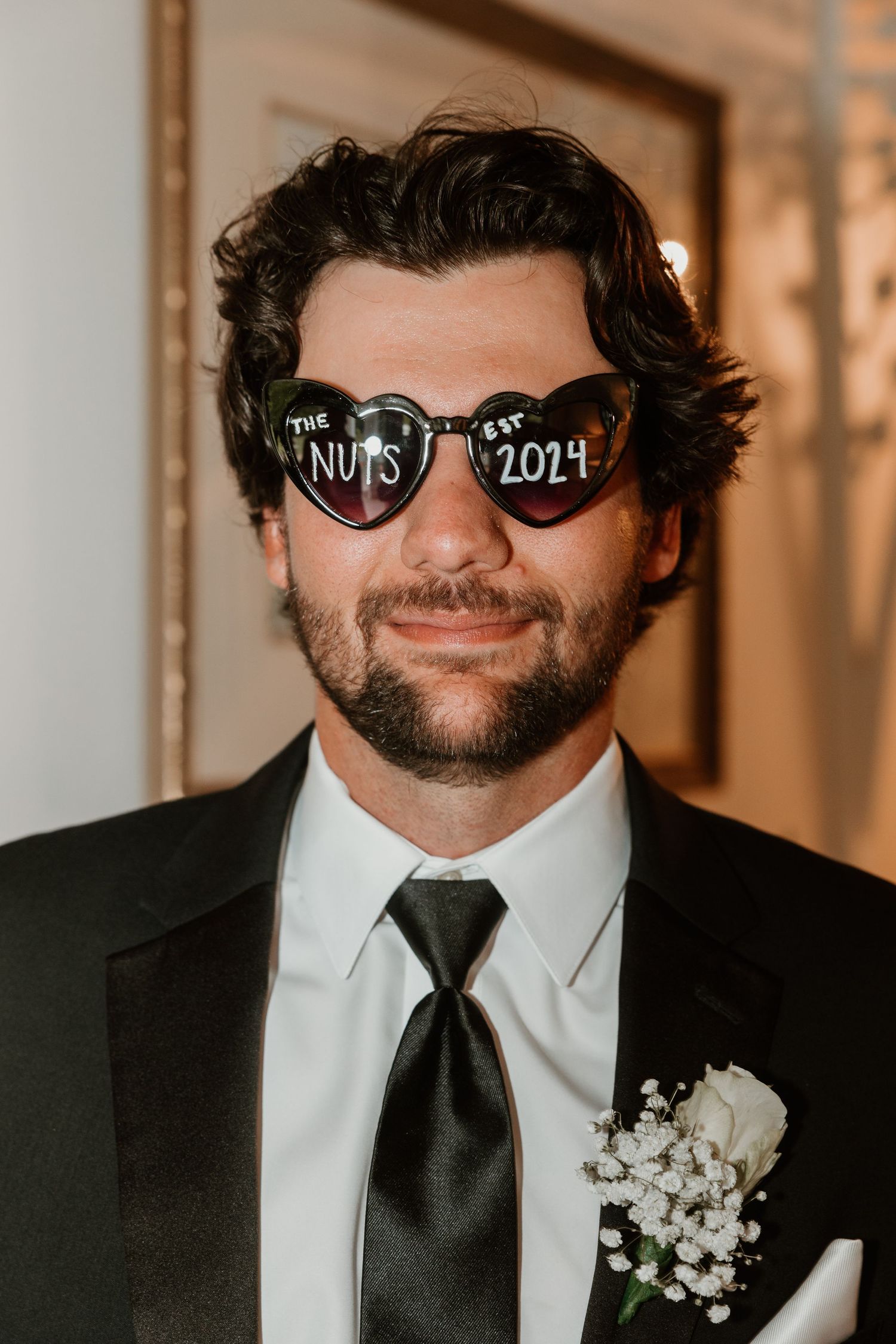 Groom wearing sunglasses with heart-shaped frames at a wedding celebration.
