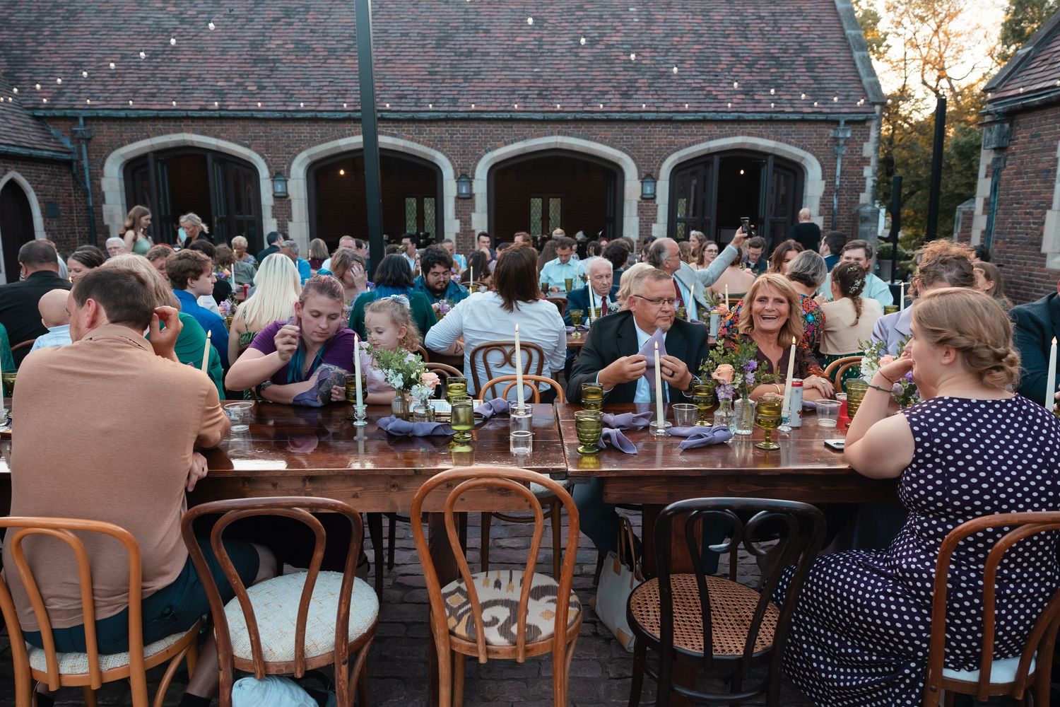 Guests seated at long outdoor dining tables during a garden party or wedding reception at dusk.