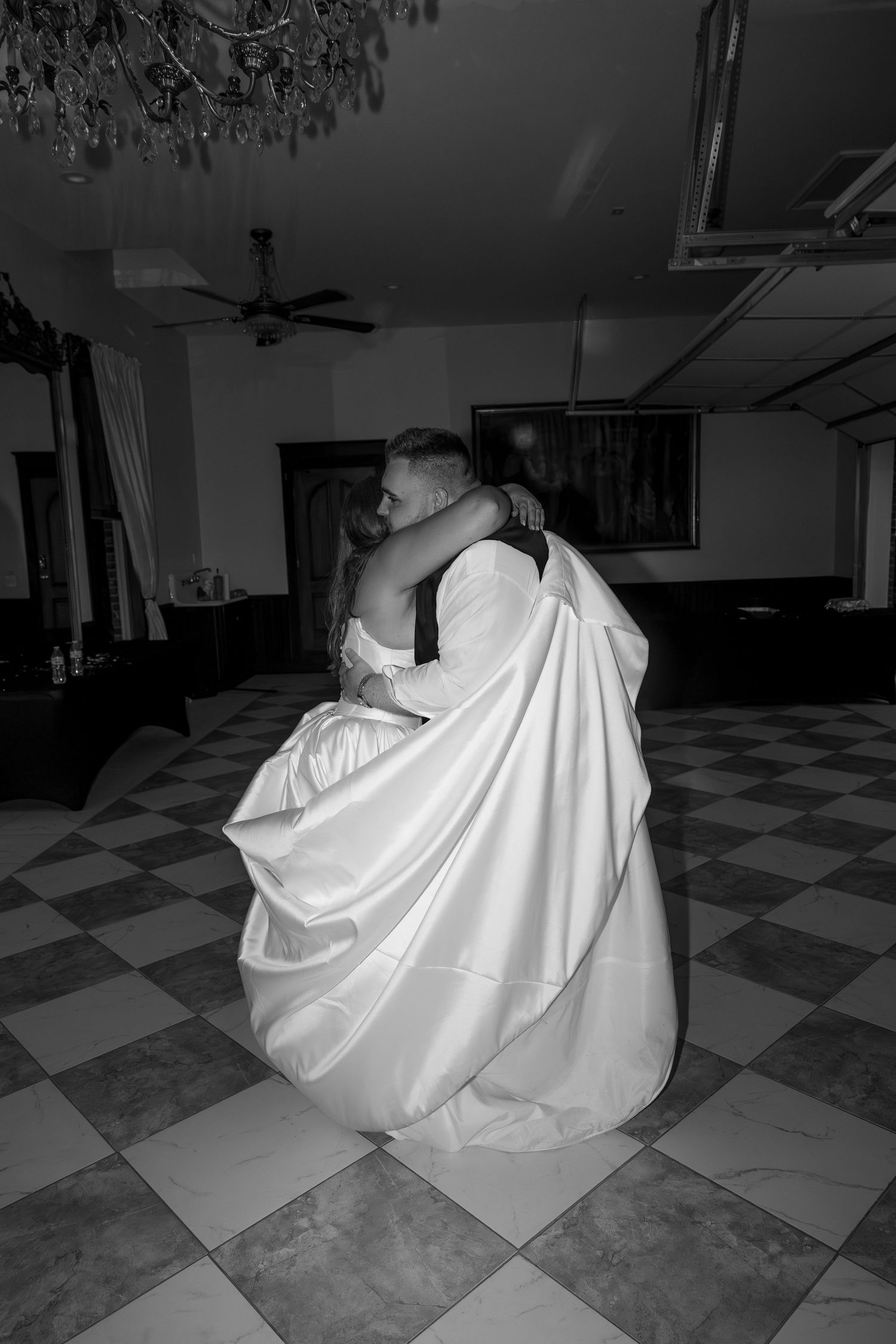 A dramatic black and white photo of dancers swirling on a checkered ballroom floor.
