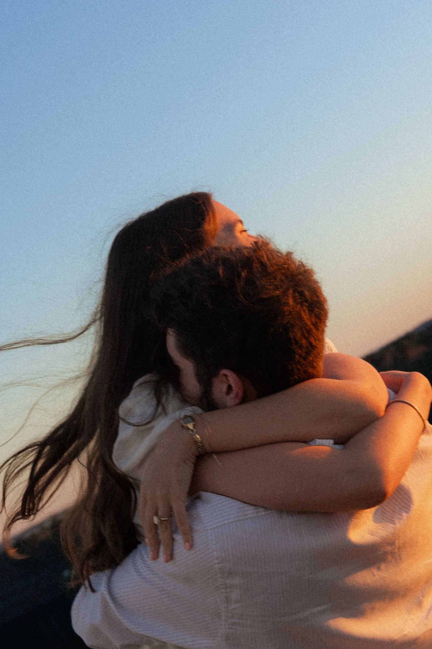 A series of silhouetted figures embracing at sunset against a soft blue sky.