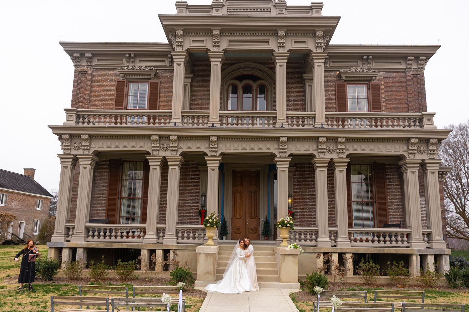 Elegant Victorian mansion with ornate columns and balconies serves as backdrop for wedding ceremony.