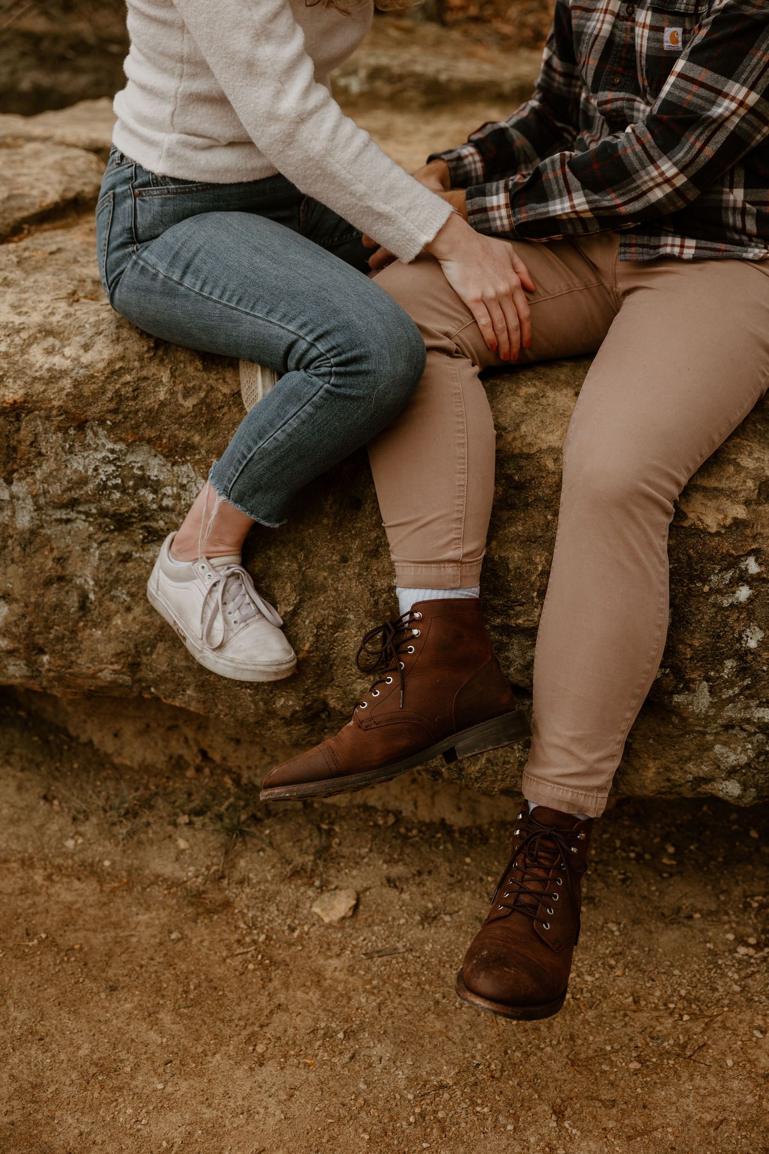 Close-up of two people's legs dangling over edge of rocky surface, wearing casual attire.