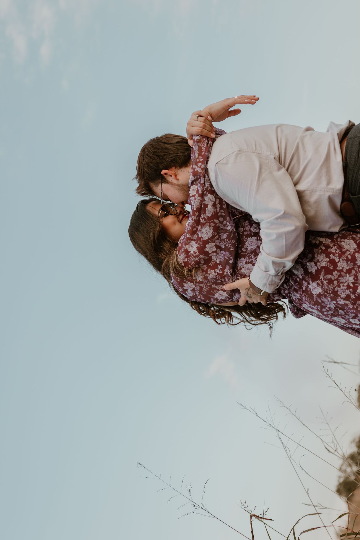 Couple in burgundy and white embracing against light blue sky background.