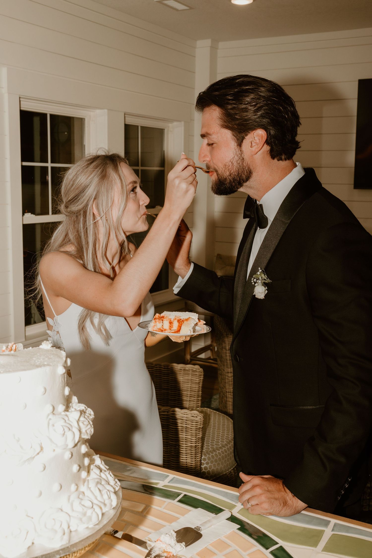 Playful moments shared between newlyweds during cake cutting ceremony at an indoor reception.